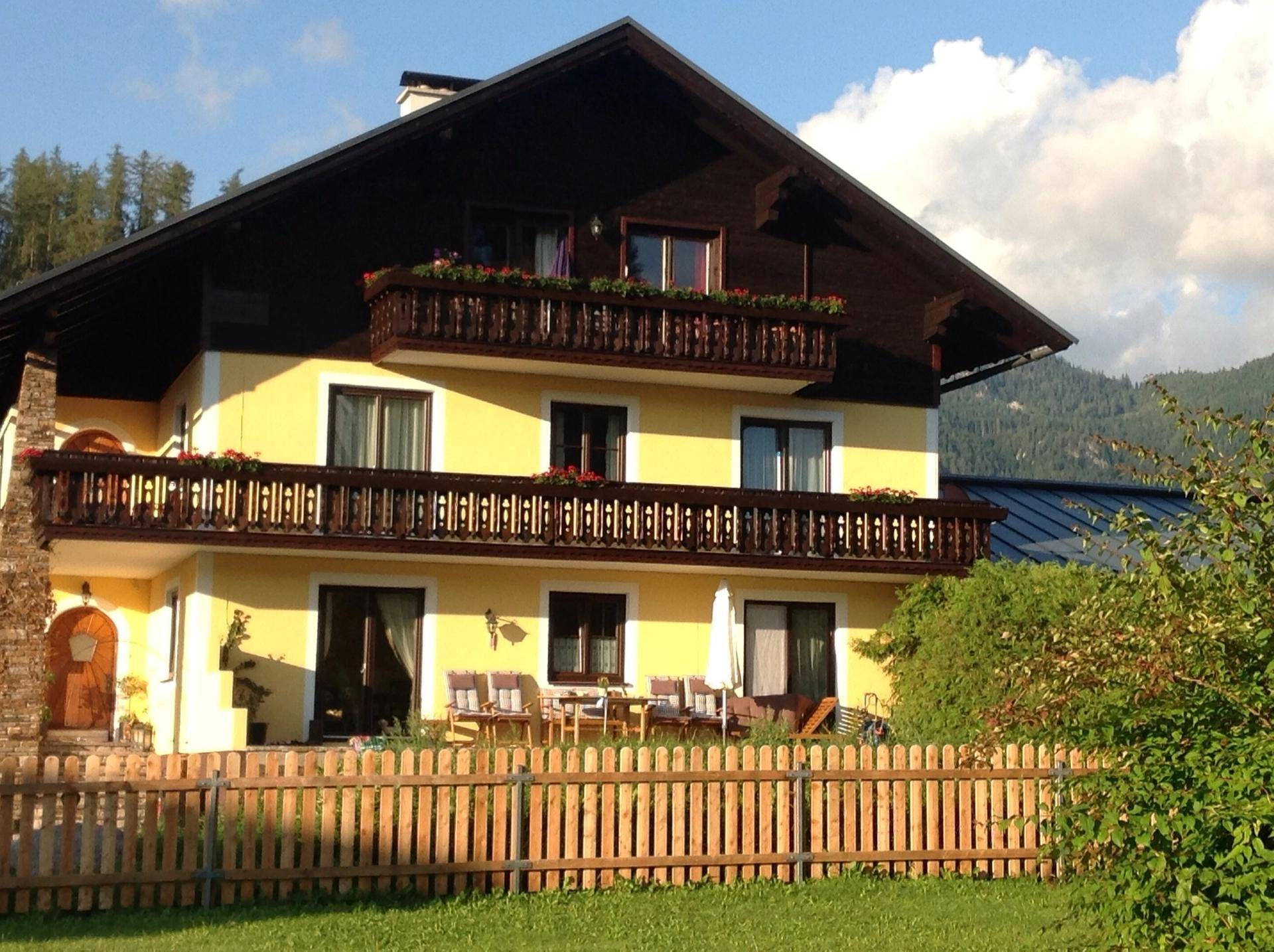 Traditionelles Haus mit gelber Fassade, Holzbalkonen und möblierter Terrasse.