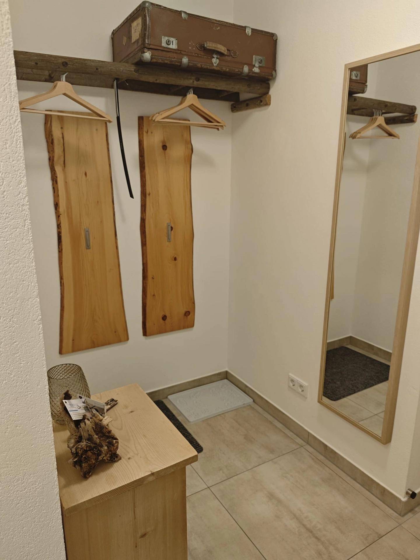 Heller Flur mit Holzbänken, großem Spiegel und rustikalen Garderobenhaken.