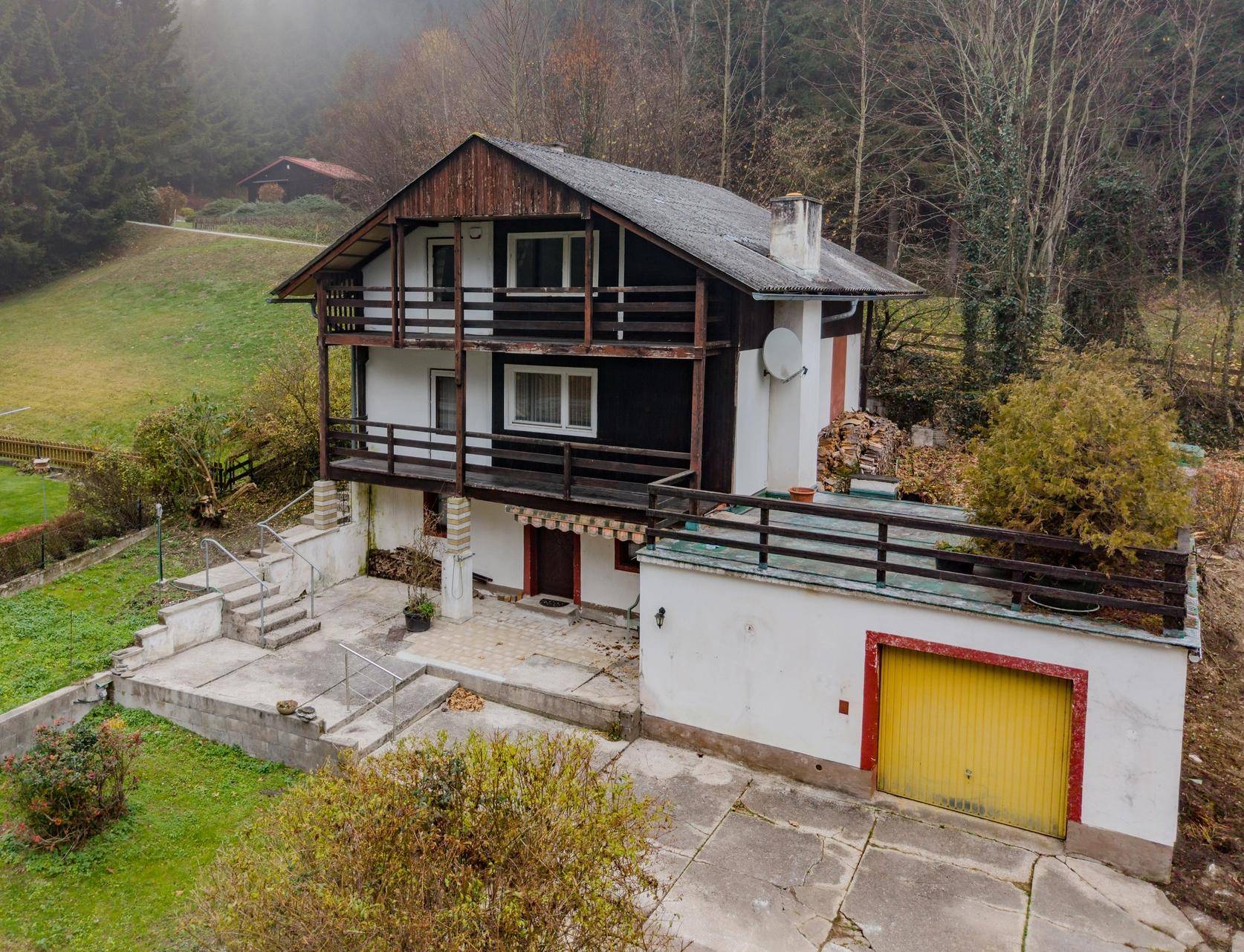 Freistehendes Haus mit Balkonen, Garage und umgebender Natur in nebliger Landschaft.