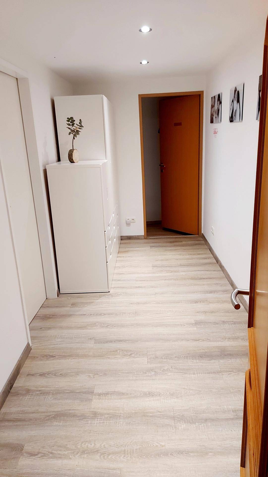 Heller Flur mit Laminatboden und weißen Wänden, der zu weiteren Räumen führt.