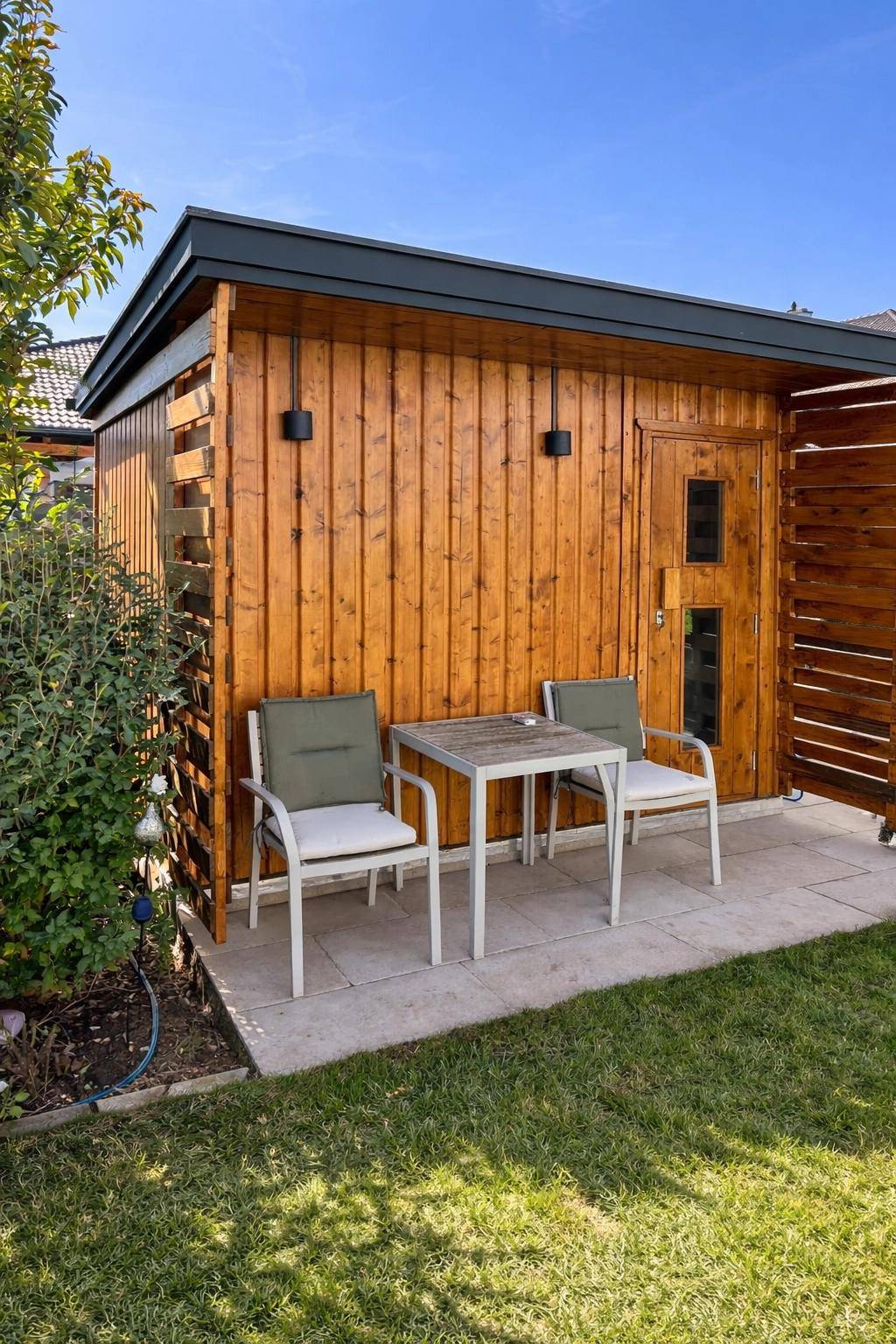 Gemütlicher Sitzbereich auf einer kleinen Terrasse neben einem Holzschuppen im Garten.