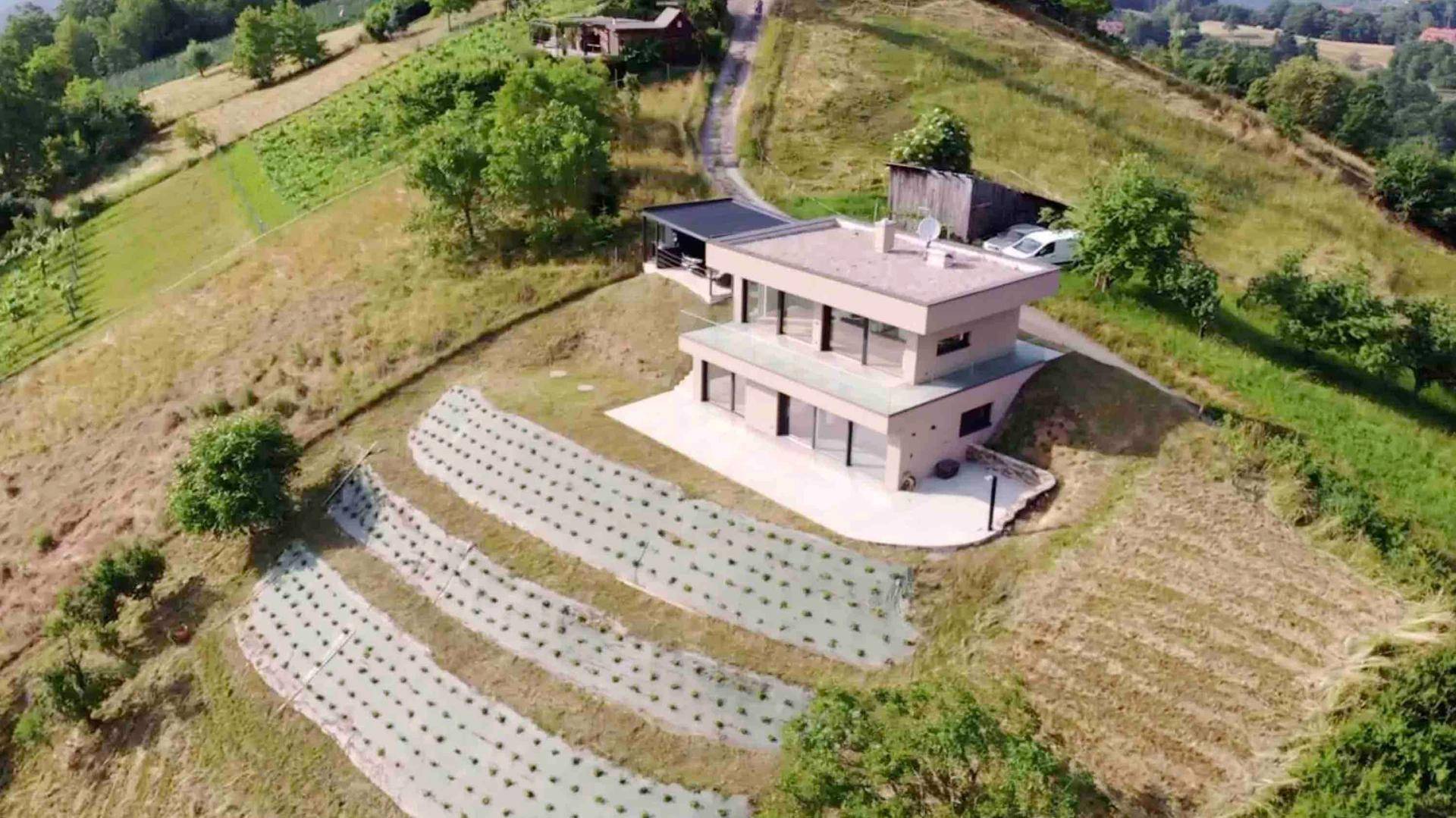 Luftaufnahme eines modernen Hauses auf einem Hügel mit terrassierten Anbauflächen und weitem Landschaftsblick.