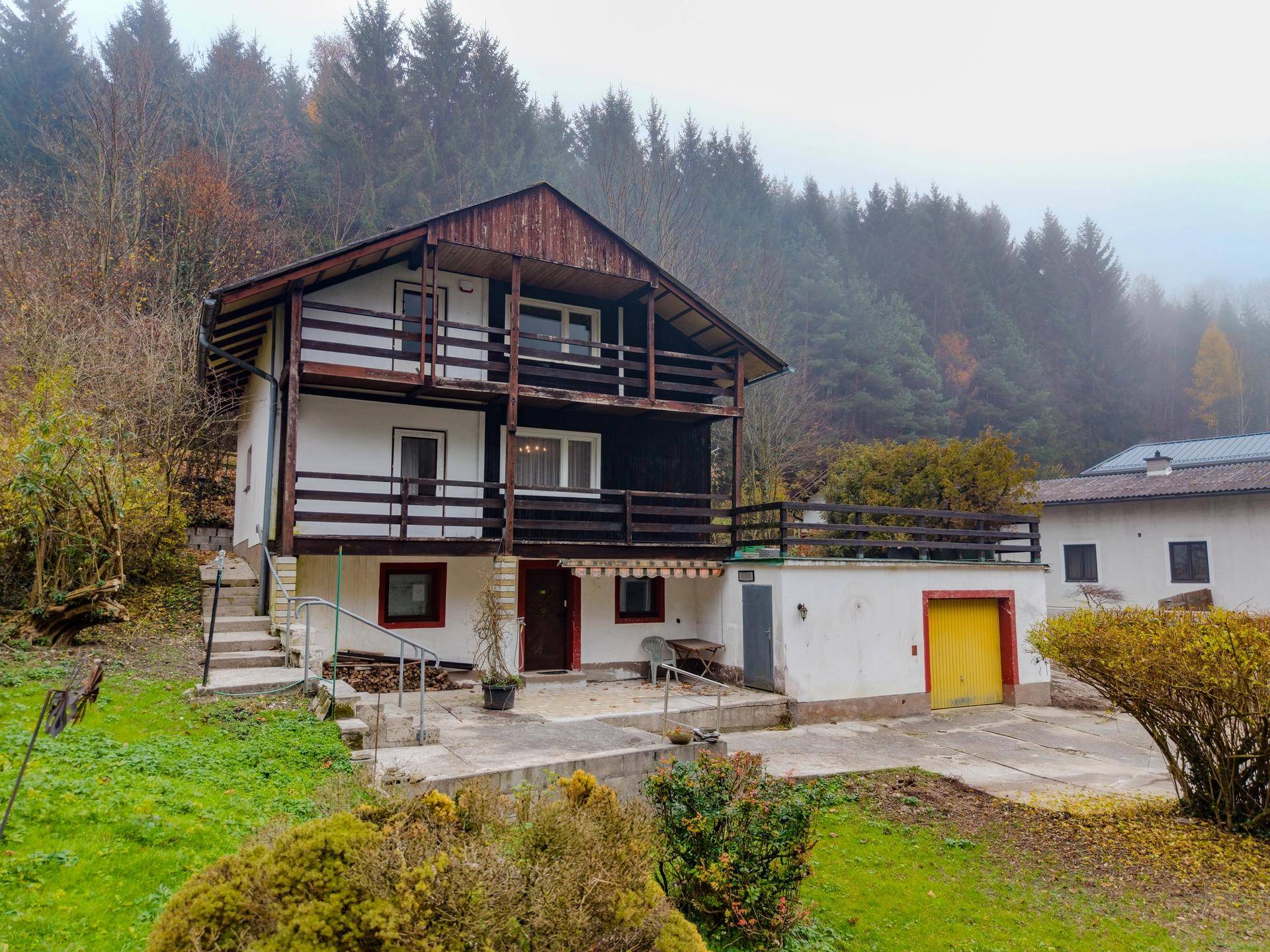 Freistehendes Haus mit Balkonen, Garage und umgebender Natur in nebliger Landschaft.