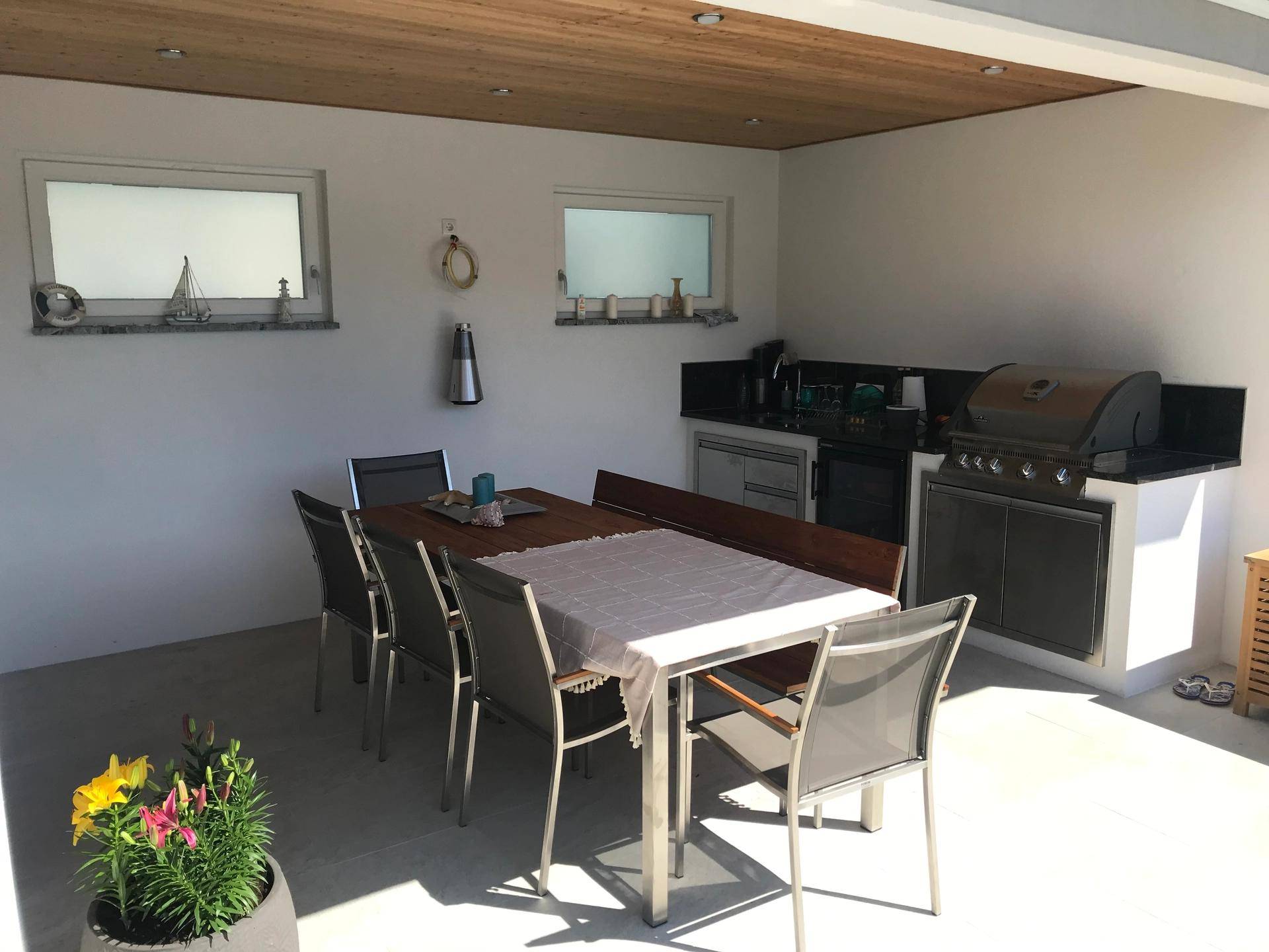 Überdachte Außenküche mit großem Esstisch, Grill und Holzdecke für gesellige Abende.