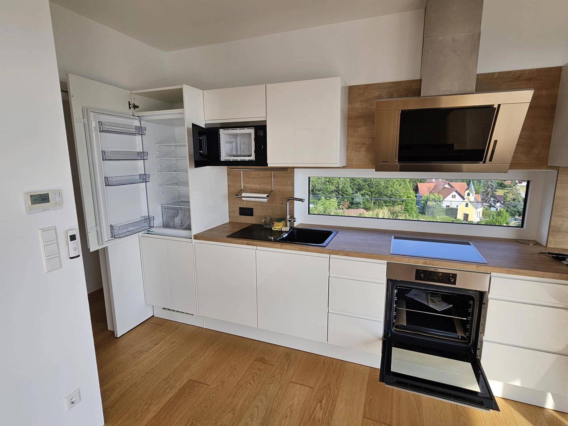 Moderne Einbauküche mit weißen Fronten, Holzarbeitsplatte und integrierten Geräten, bietet einen schönen Ausblick.