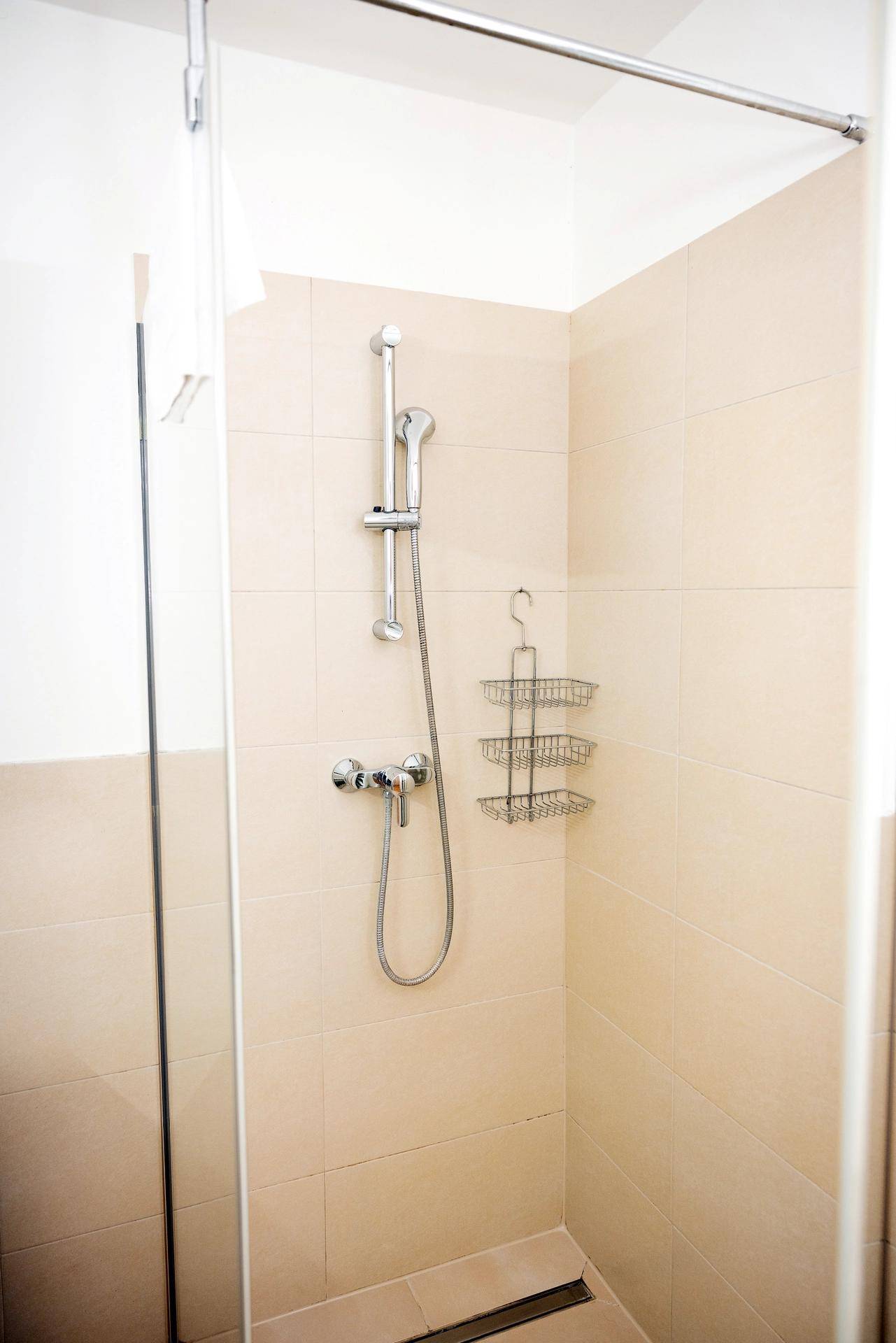Detaillierte Ansicht einer modernen Duschkabine mit beigefarbenen Fliesen und Handbrause.