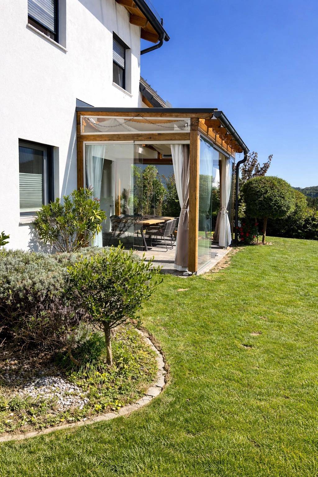 Verglaste Terrasse mit Esstisch und Stühlen, umgeben von einem gepflegten Garten.