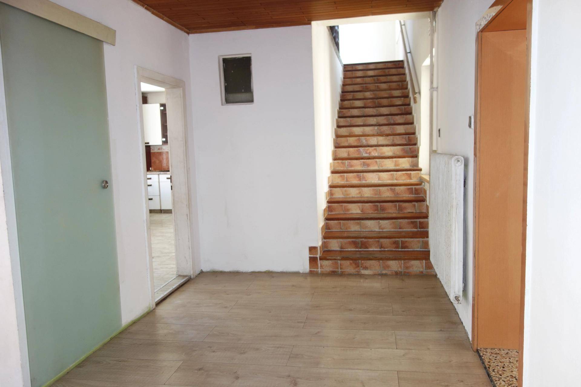 Flur mit hellem Laminatboden, weiß gestrichenen Wänden und einer gefliesten Treppe ins Obergeschoss.