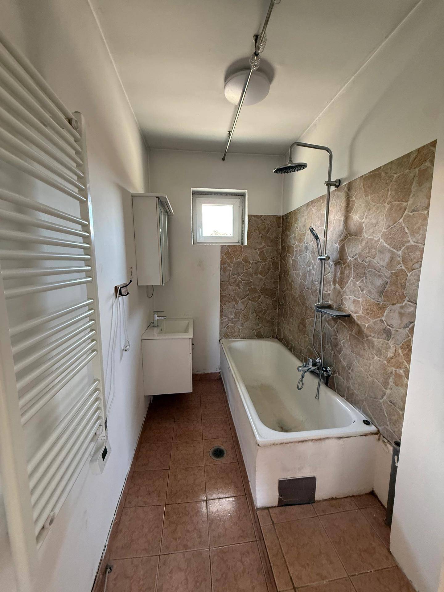 Badezimmer mit Badewanne, Dusche, Waschbecken und Fliesenboden, bereit für Modernisierung.