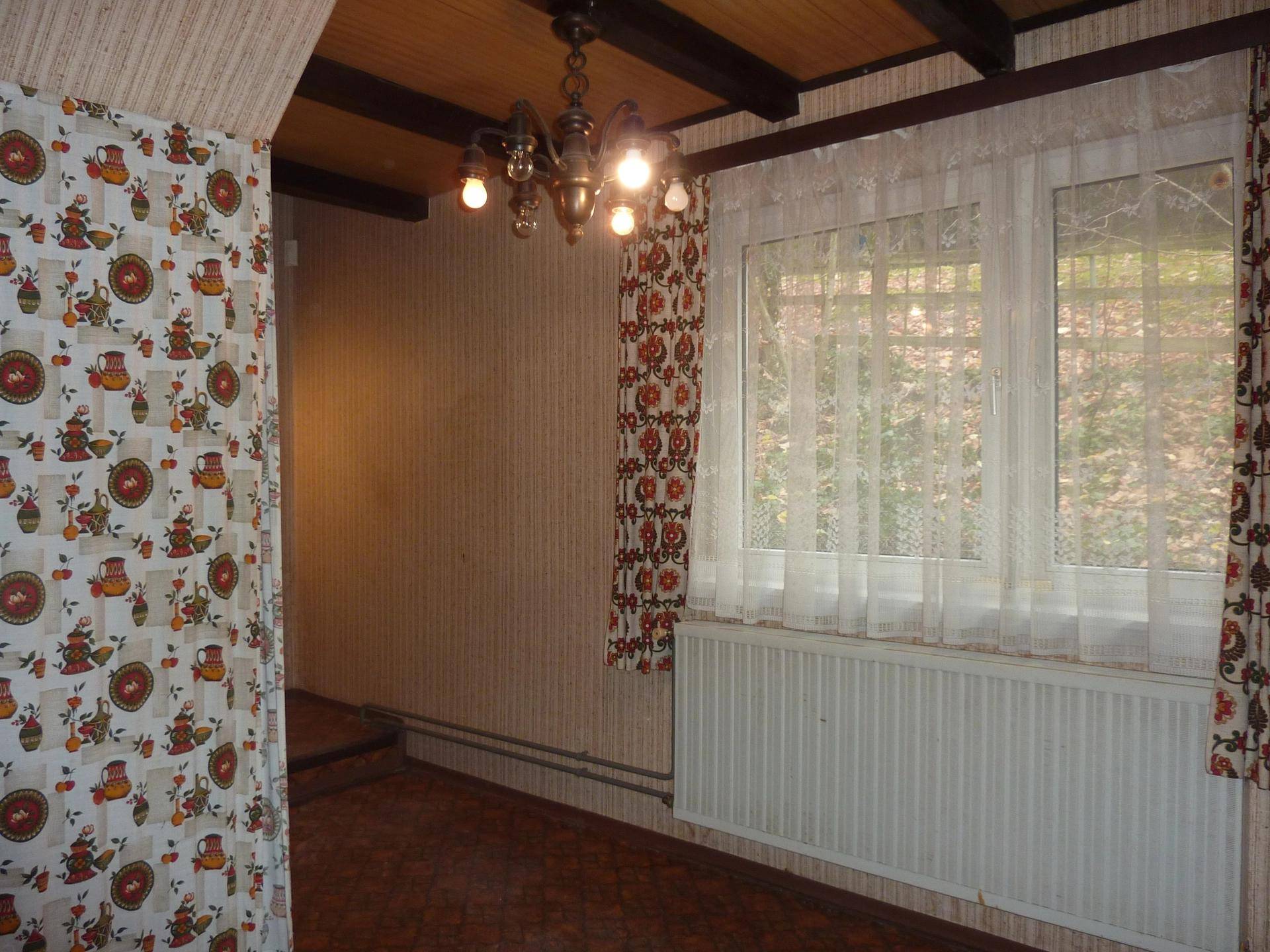 Flur mit gemusterter Tapete, Holzdecke und Fenster mit Blick ins Grüne.