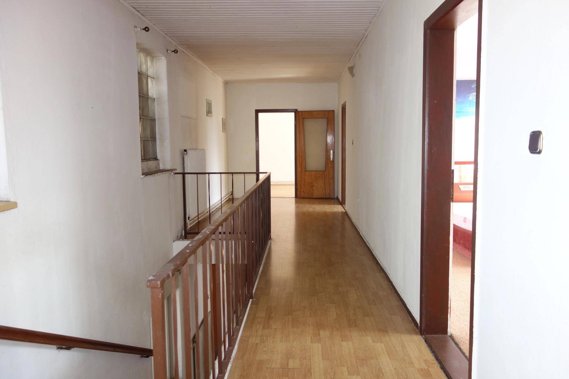 Langer Flur mit hellem Laminatboden, weißen Wänden und einem Holzgeländer.