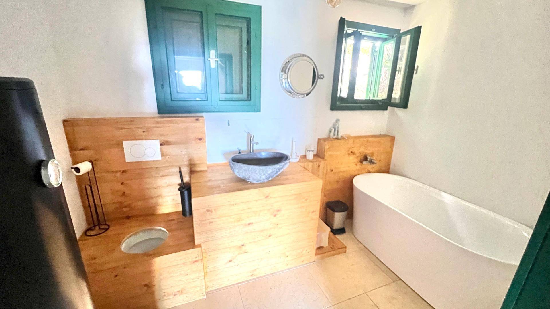 Modernes Badezimmer mit freistehender Badewanne, Holzverkleidung und Steinwaschbecken, hell und einladend.