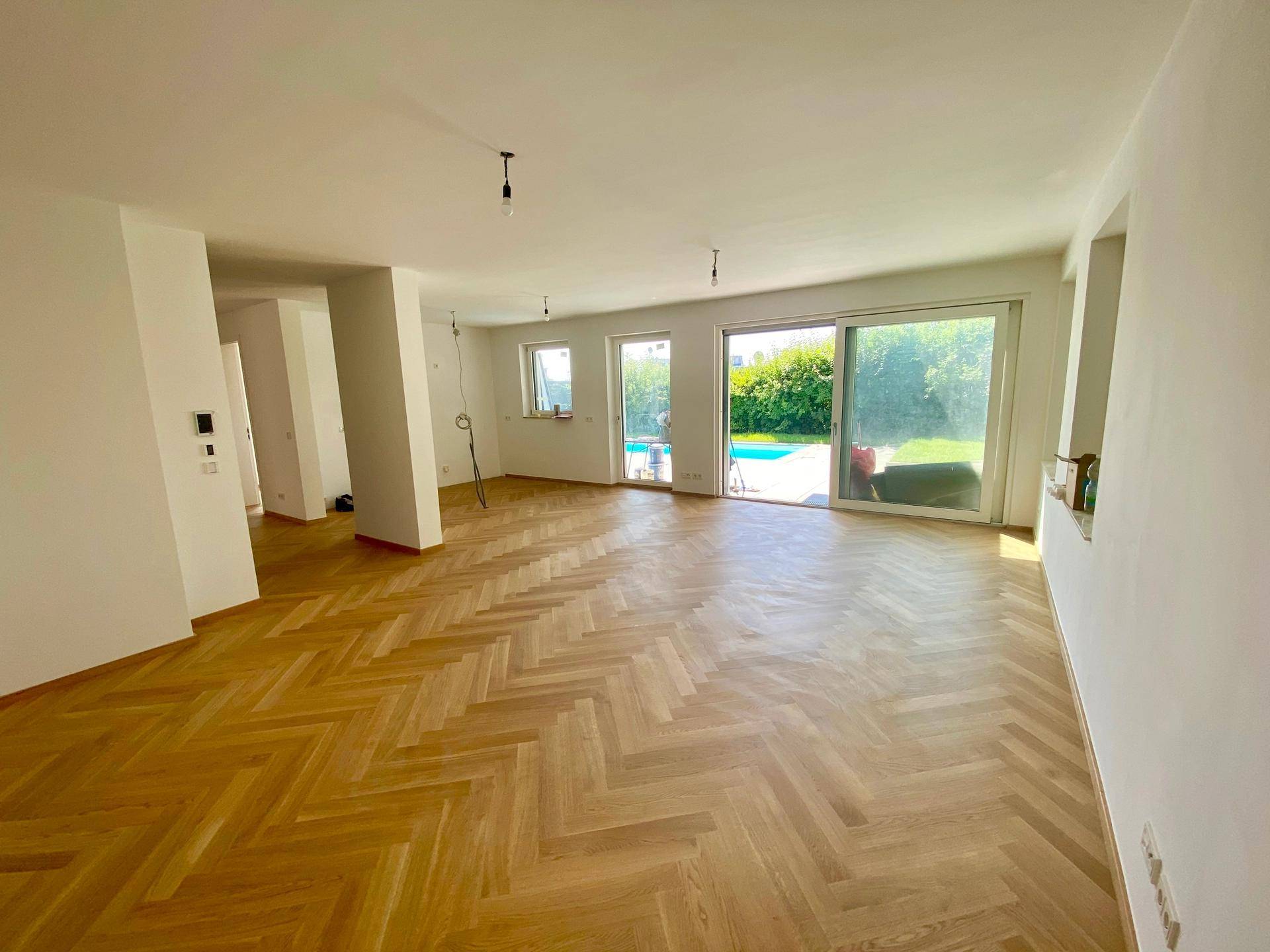 Heller, offener Wohnbereich mit Fischgrätparkett und Zugang zum Garten mit Pool.
