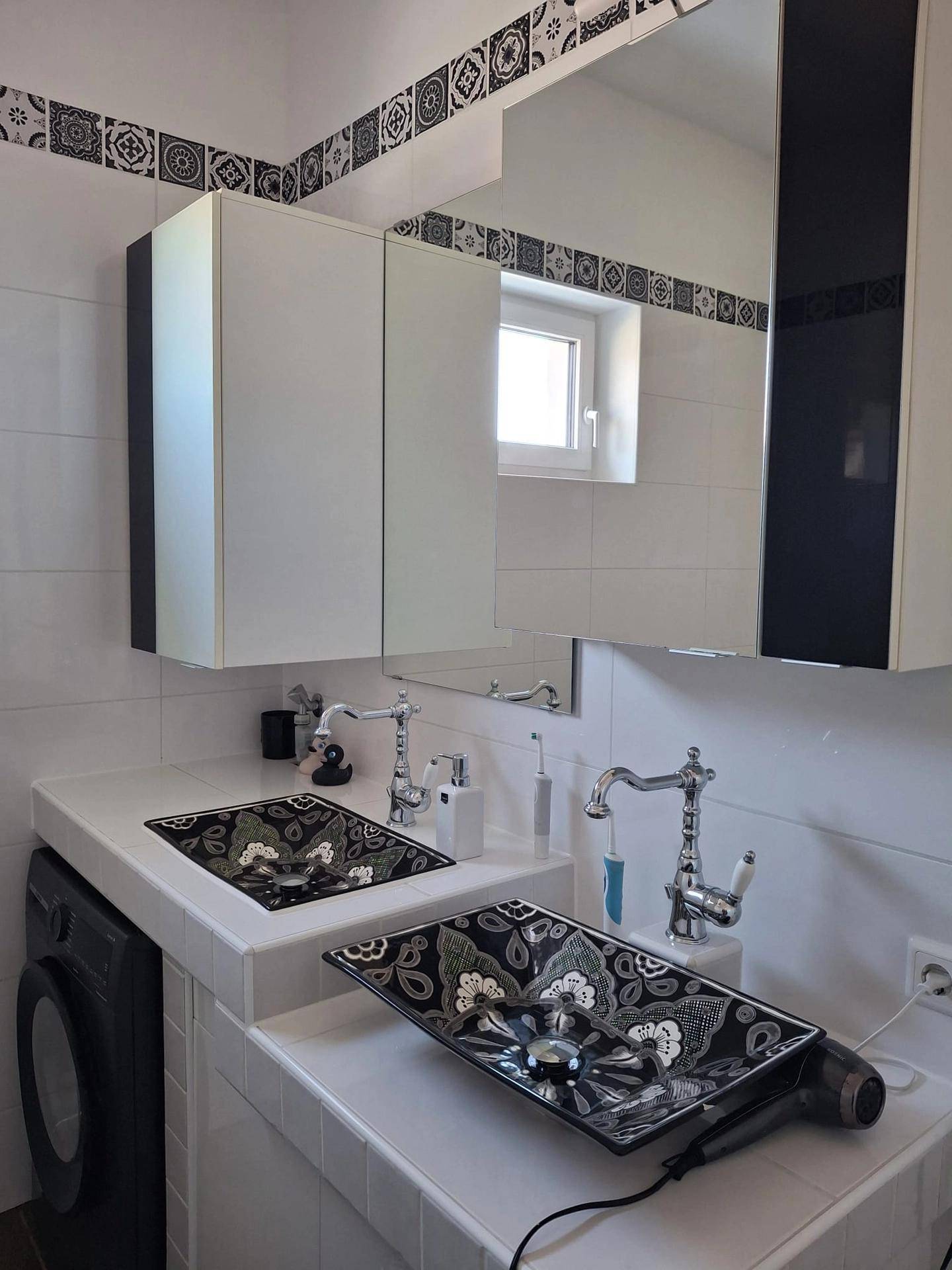 Badezimmer mit zwei einzigartigen Waschbecken, Spiegelschrank und Fenster für Tageslicht.