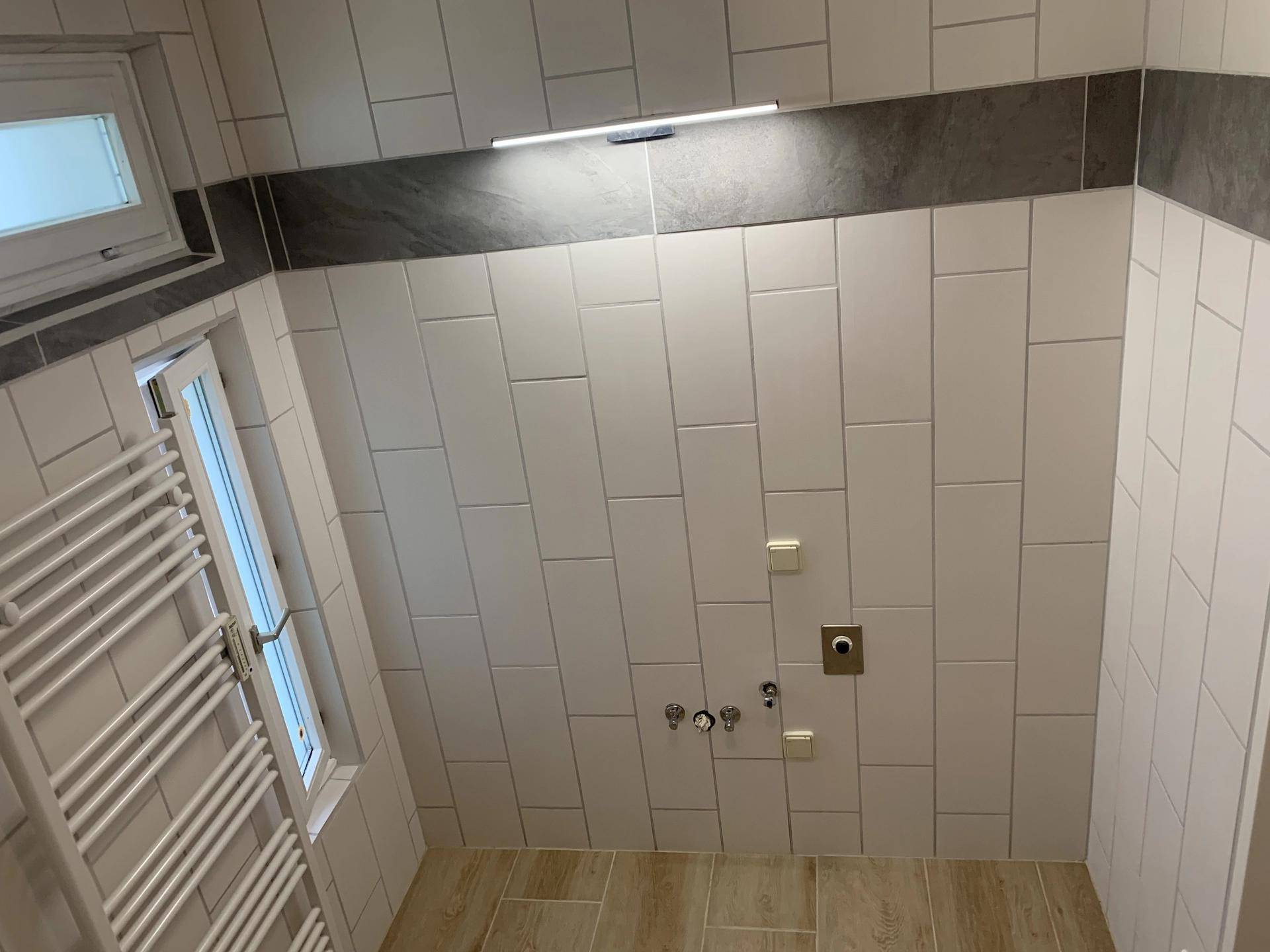 Helles Badezimmer mit Fenster, beheiztem Handtuchhalter und modernen Wandfliesen.