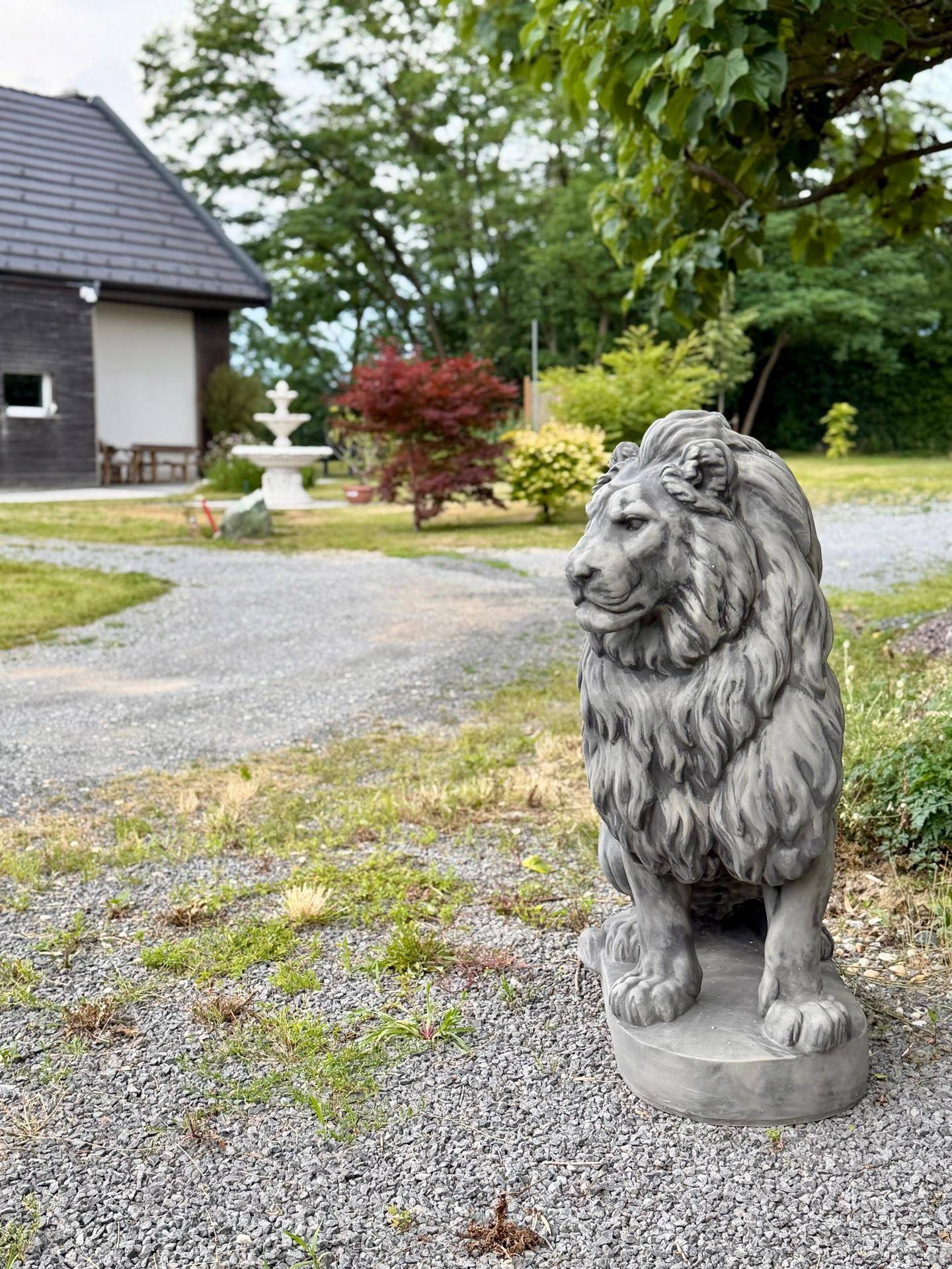 Gartenweg aus Kies mit einer dekorativen Löwenstatue und Blick auf das Anwesen im Hintergrund.