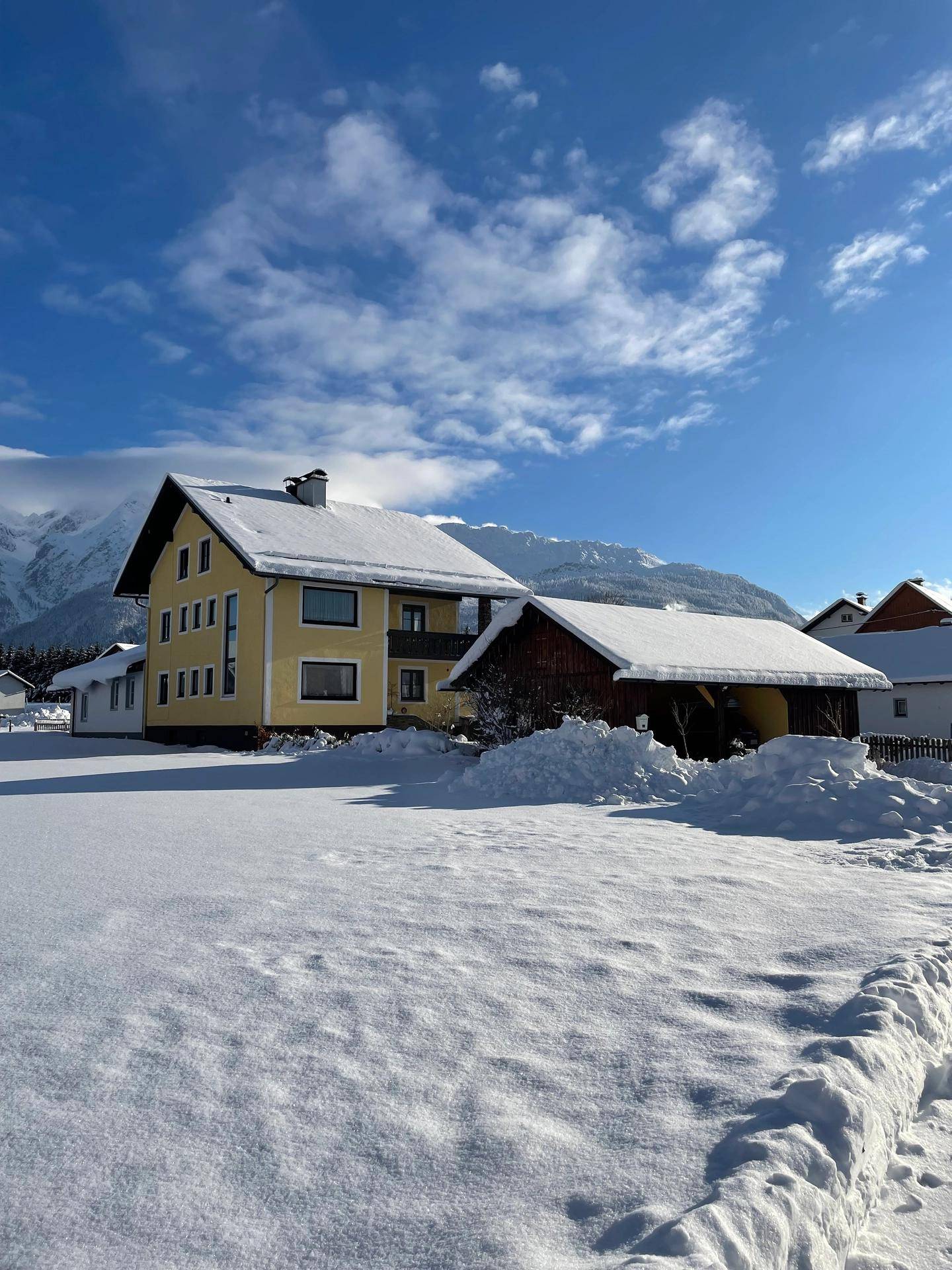 Traditionelles Haus mit gelber Fassade und schneebedeckter Landschaft im Winter.