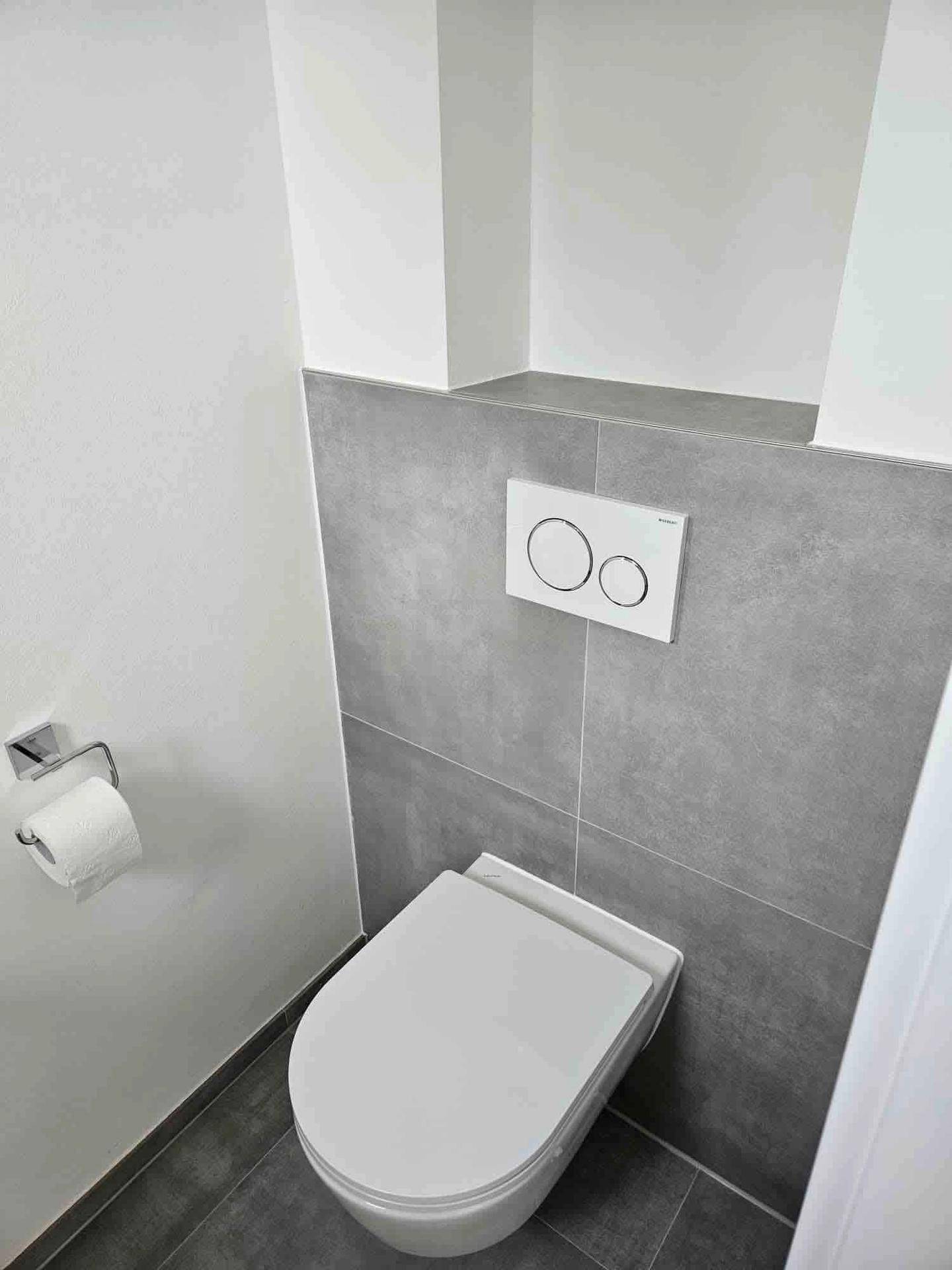 Modernes WC mit wandhängender Toilette und grauen Fliesen, minimalistisch und funktional gestaltet.