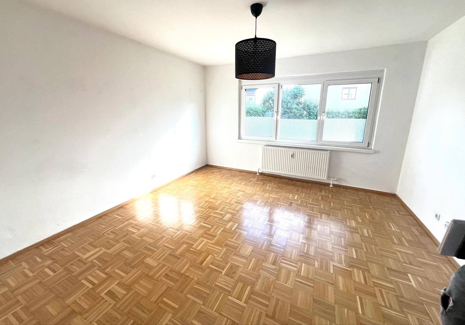 Helles Zimmer mit Parkettboden, großen Fenstern und Blick ins Grüne.