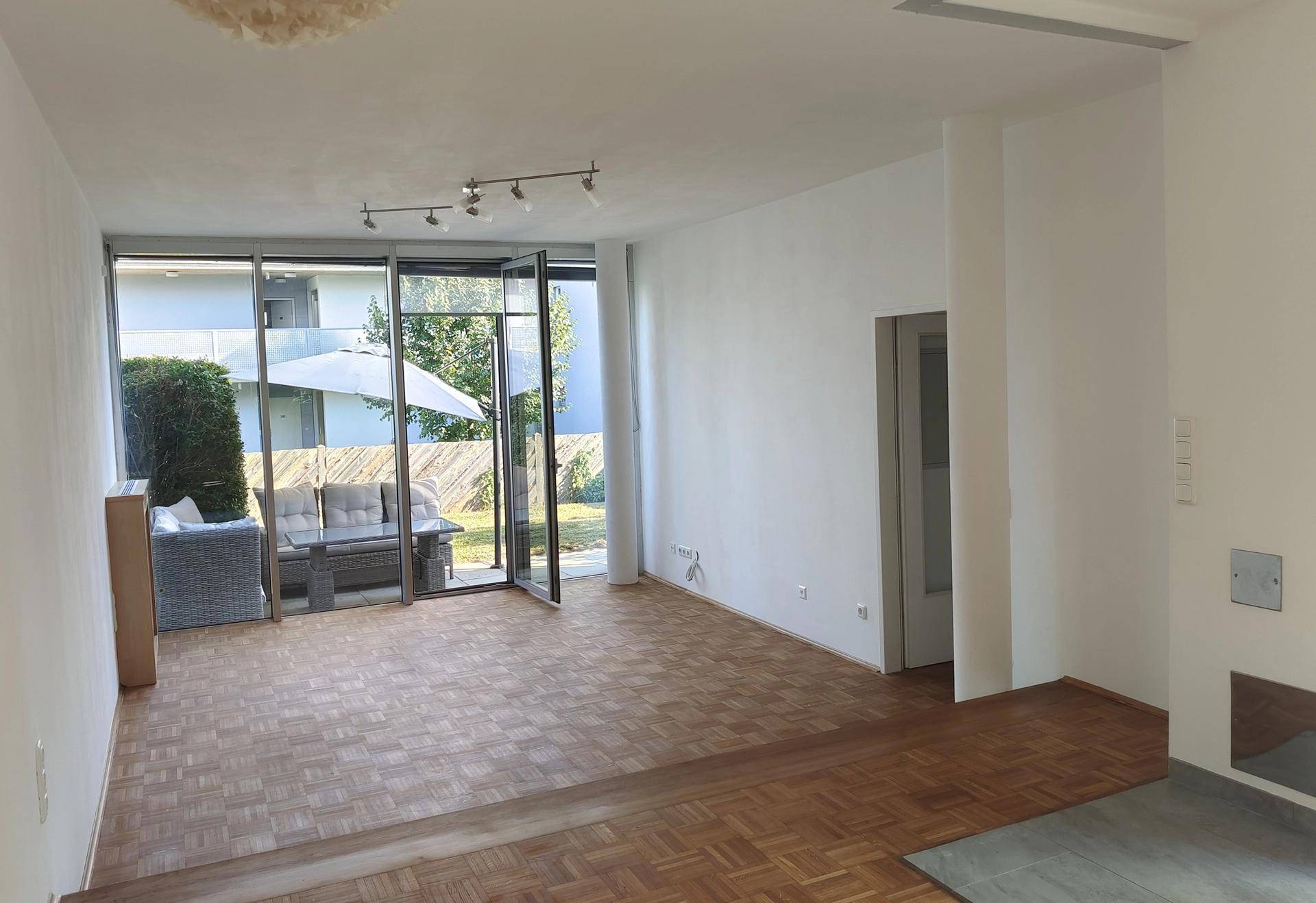 Geräumiges Wohnzimmer mit großen Fenstern, die viel Tageslicht hereinlassen und Zugang zur Terrasse bieten.