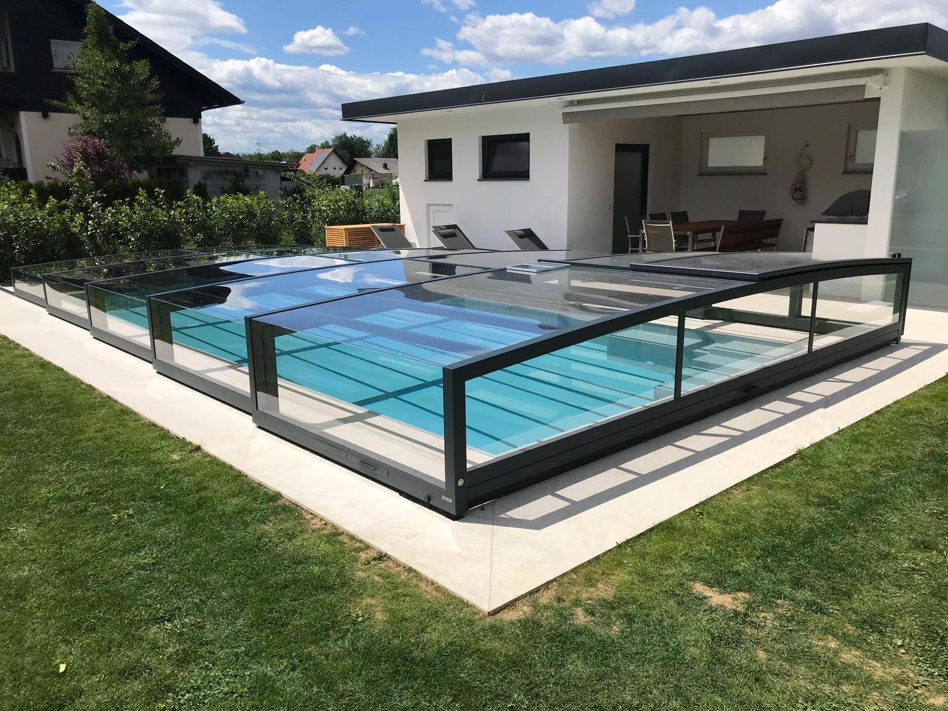 Moderner Pool mit transparenter Abdeckung, umgeben von Rasen und einer kleinen Pool-Lounge.