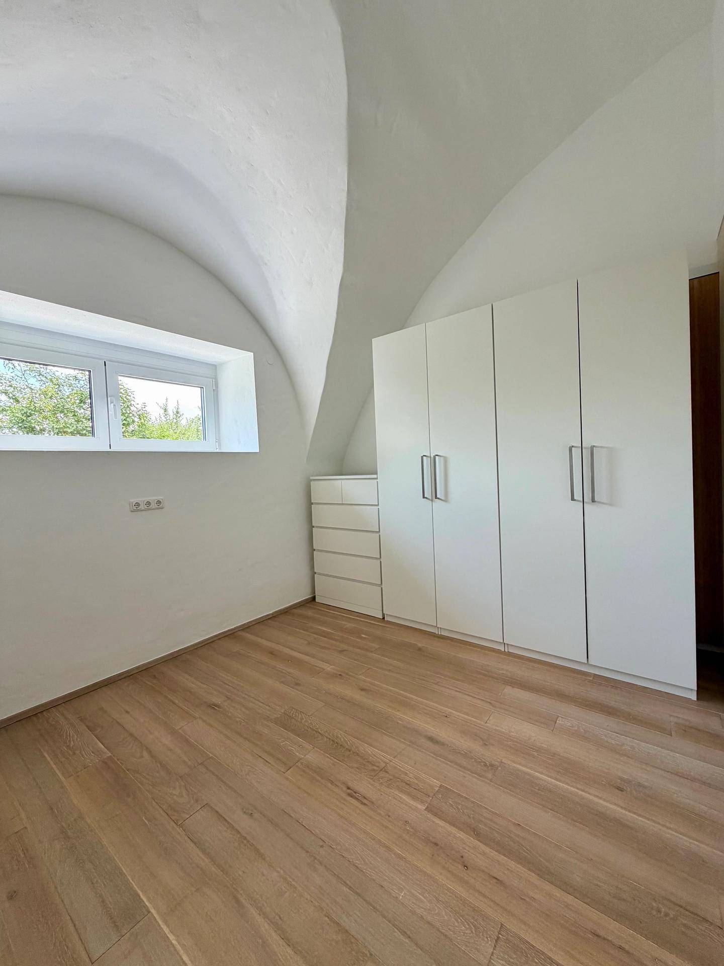 Helles Schlafzimmer mit gewölbter Decke, Holzboden und modernen Einbauschränken.