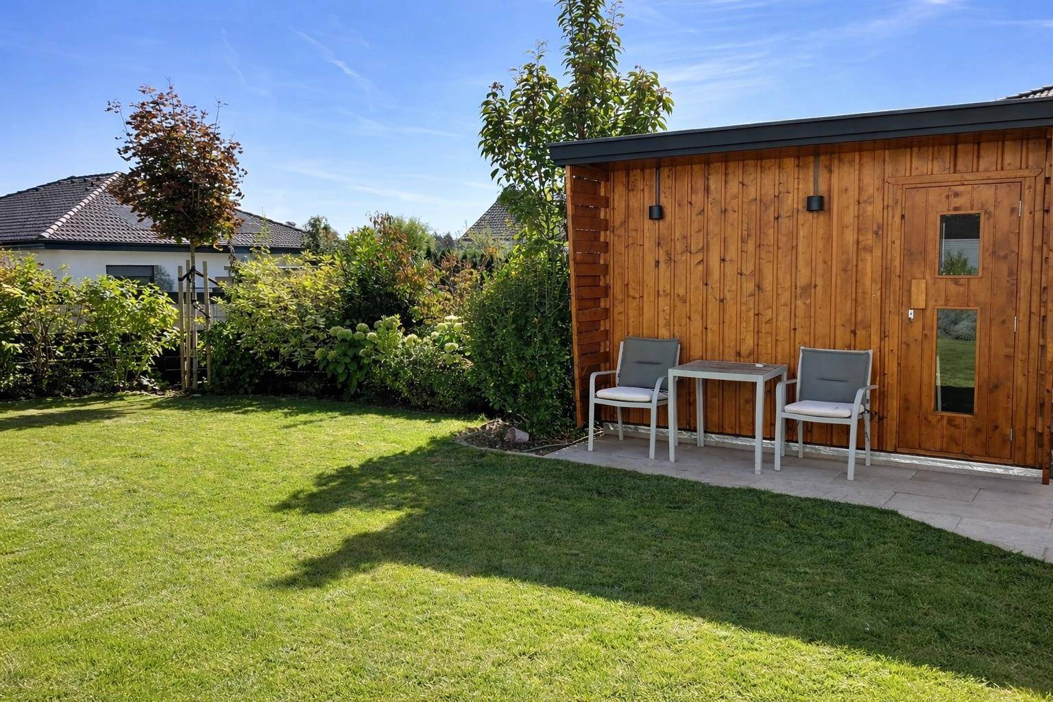 Weitläufiger Garten mit Rasenfläche und einem kleinen Sitzbereich neben einem Holzschuppen.