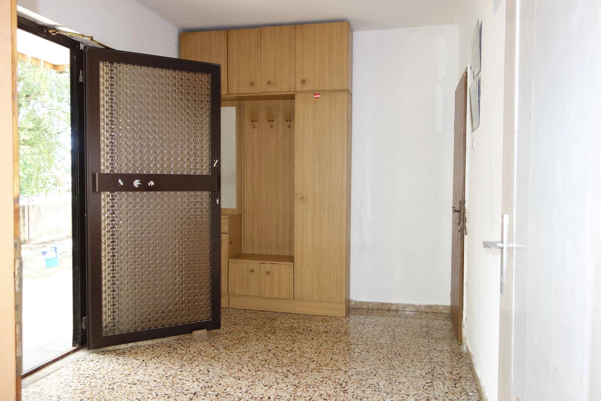 Eingangsbereich mit Terrazzoboden, weißer Wand und einem hellen Holzschrank mit Garderobe.