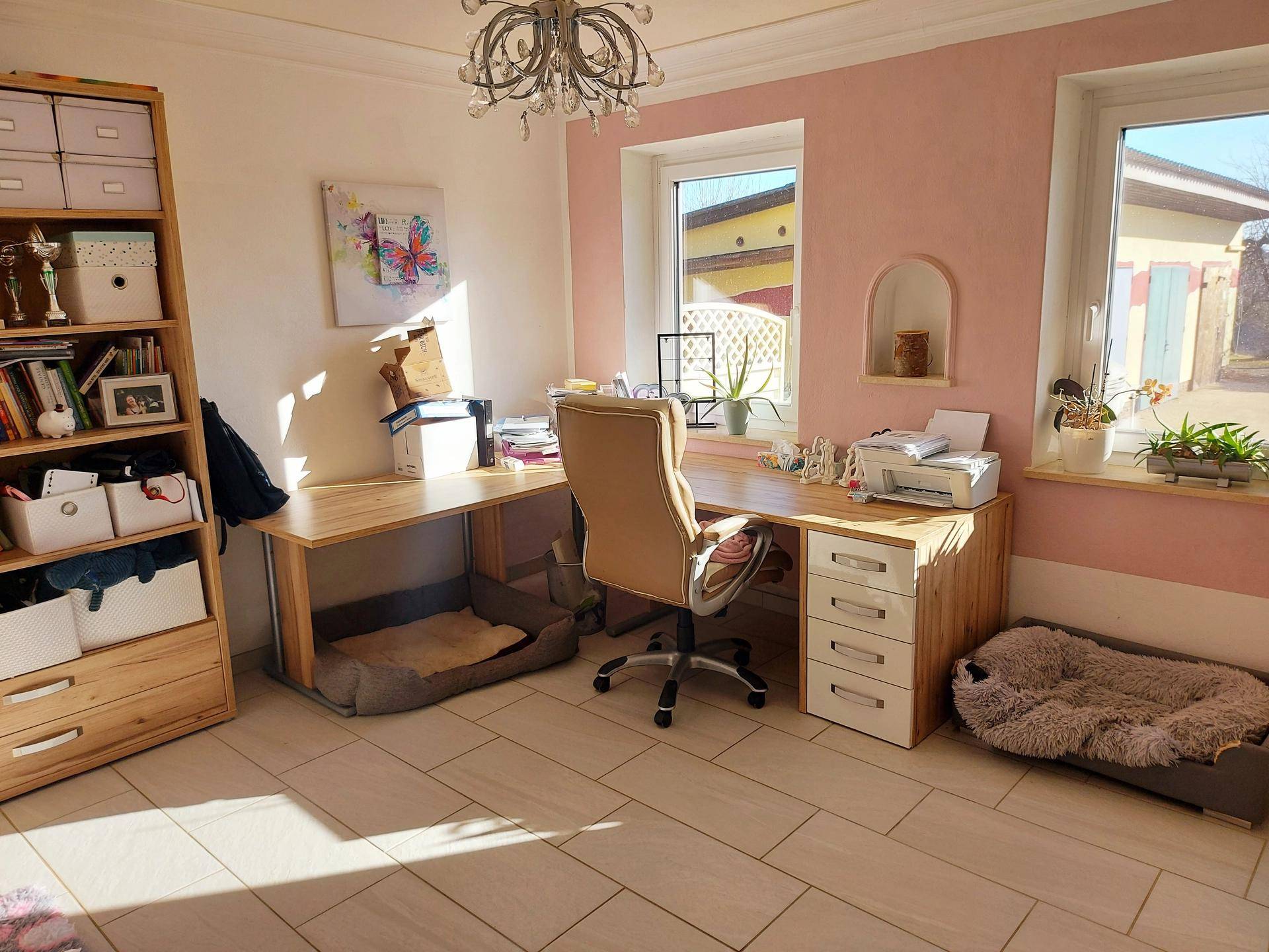Helles Arbeitszimmer mit großem Schreibtisch, Regal und rosa Wänden, ideal für Home-Office.