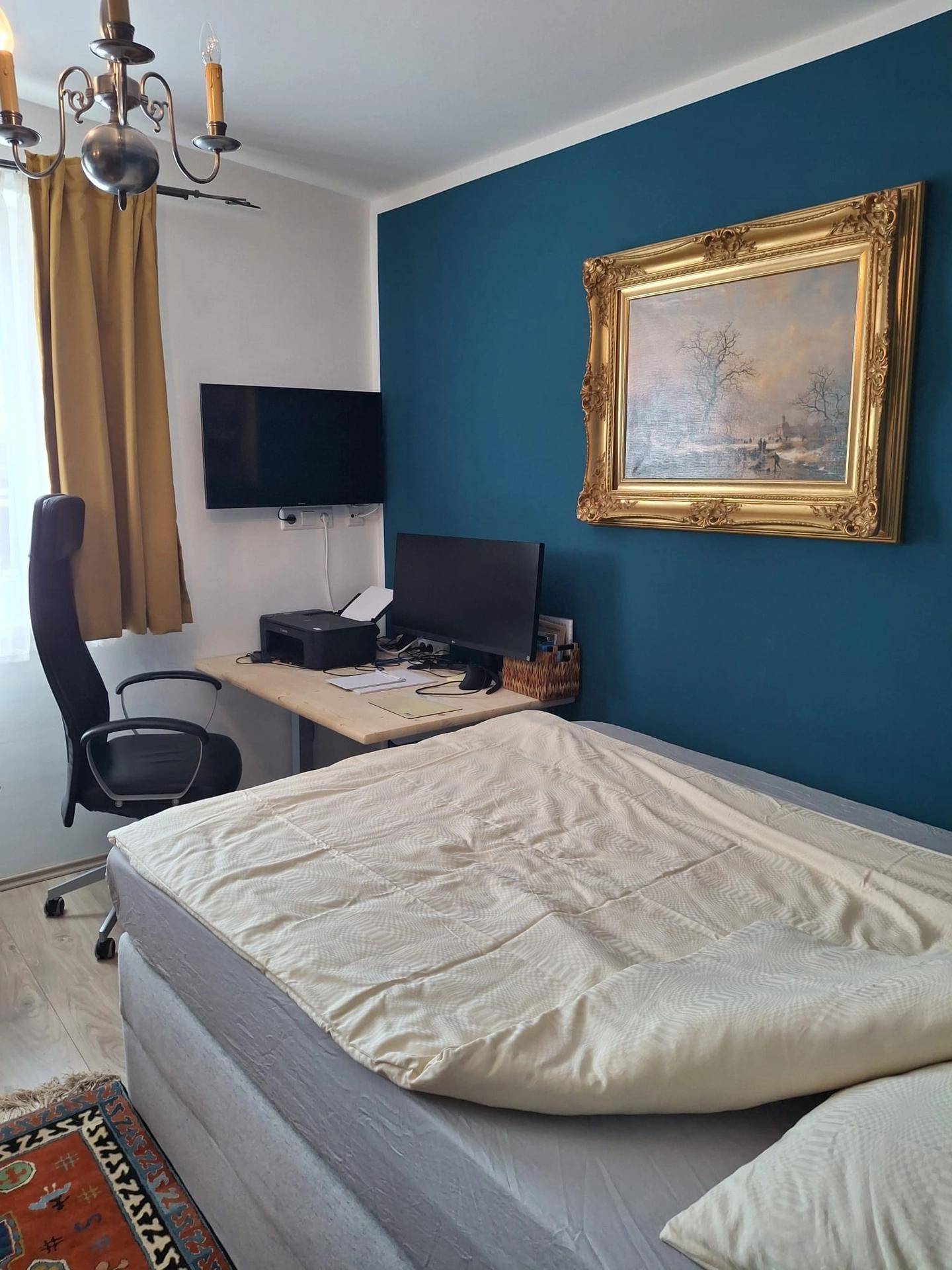 Schlafzimmer mit blau gestrichener Akzentwand, Bett und einem Arbeitsbereich mit Schreibtisch.