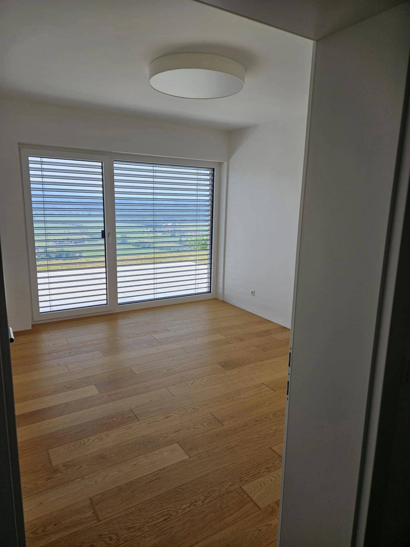 Helles Schlafzimmer mit Holzboden und großen Fenstern, die einen weiten Blick auf die Landschaft ermöglichen.