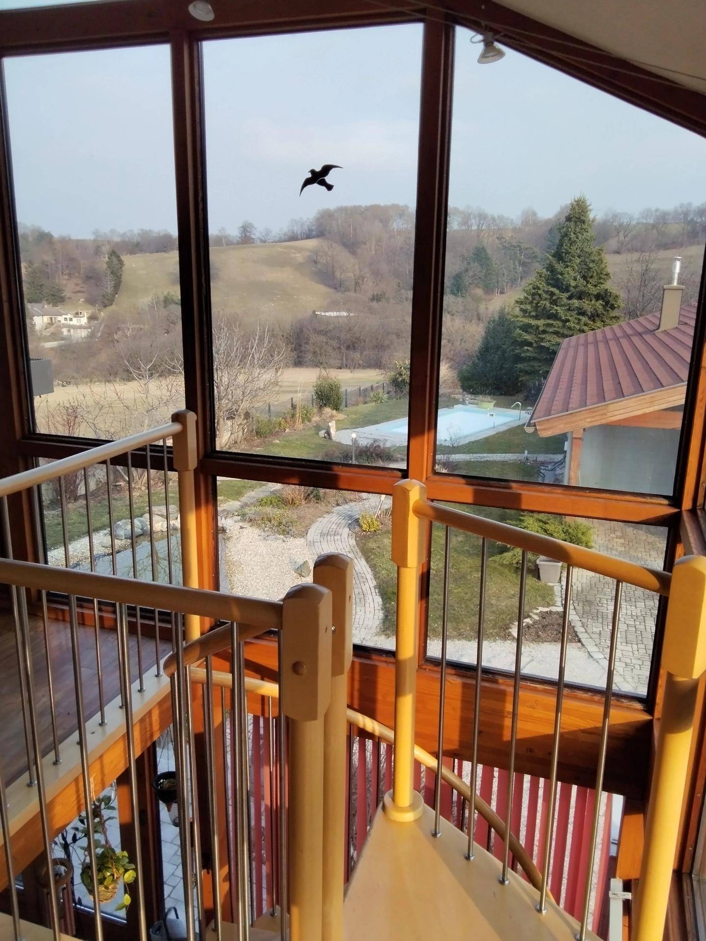 Treppenhaus mit Holzgeländer, großen Fenstern und weitem Blick über die Landschaft.