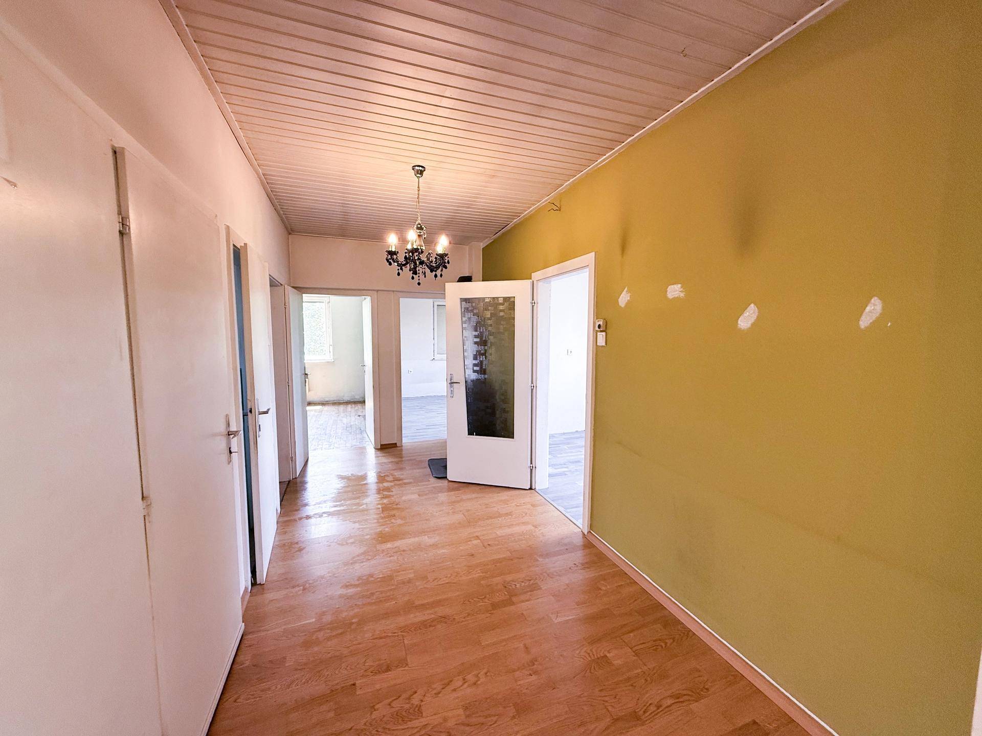 Langer Flur mit Holzboden, grüner Wand und mehreren Türen, die zu anderen Räumen führen.