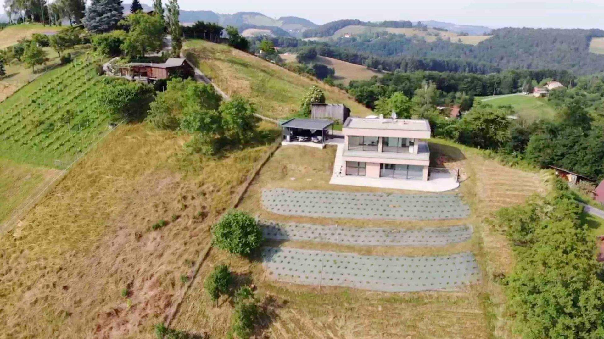 Luftaufnahme eines modernen Hauses mit Carport, umgeben von terrassierten Feldern und grünen Hügeln.
