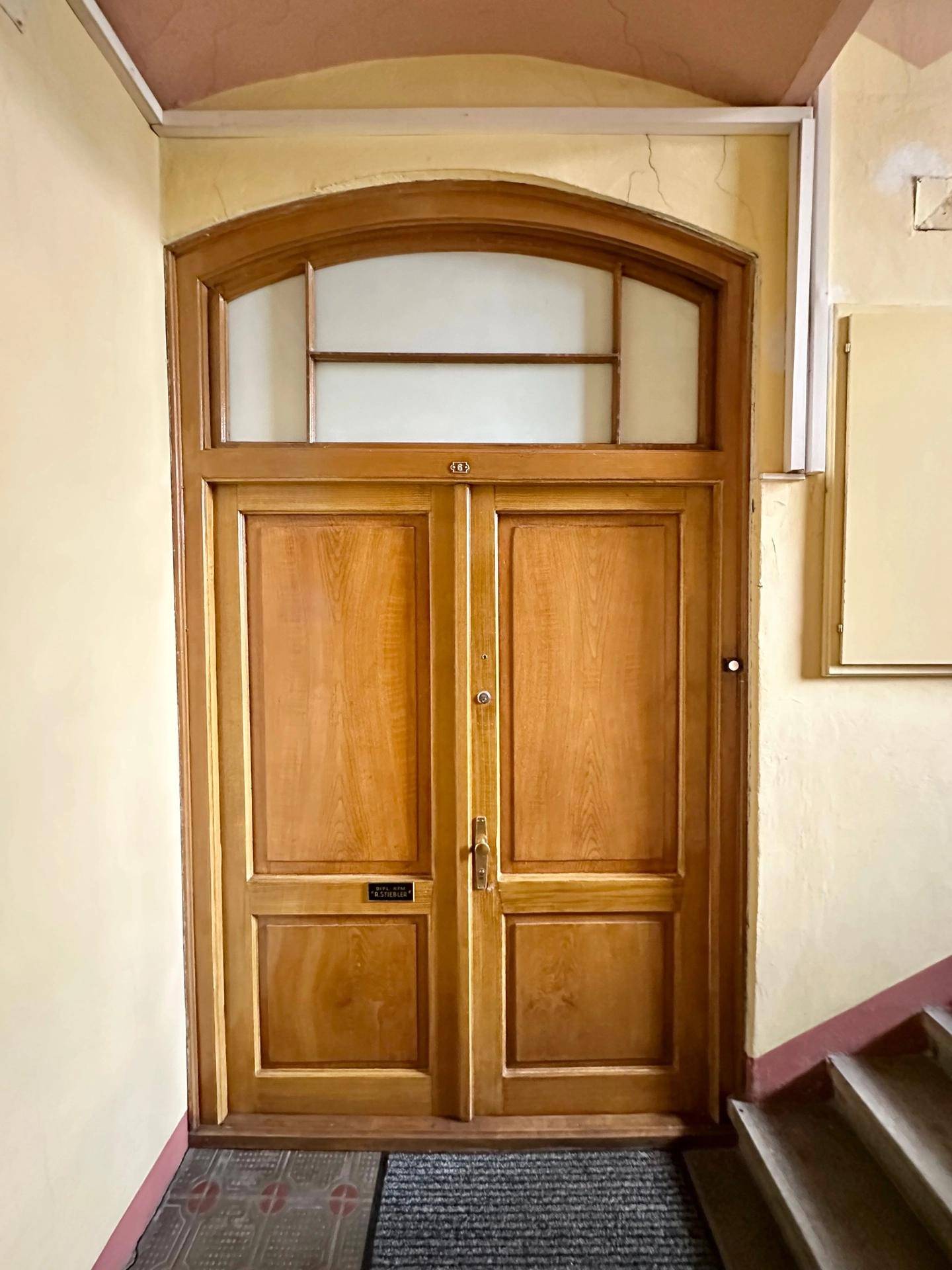 Holzeingangstür mit Oberlicht in einem historischen Treppenhaus.