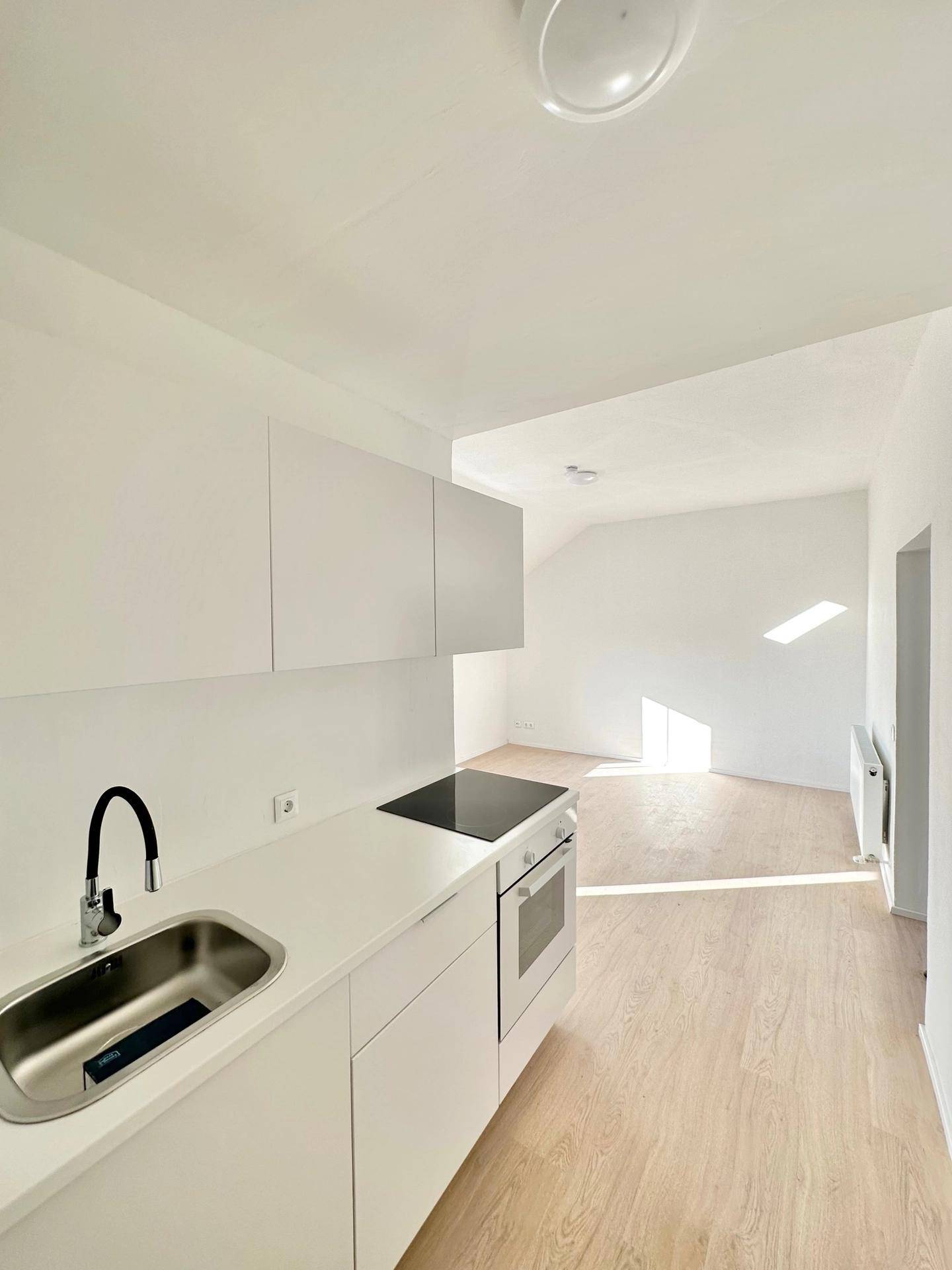 Moderne, helle Küchenzeile mit weißen Schränken, Spüle und Kochfeld in einem Dachgeschossraum.