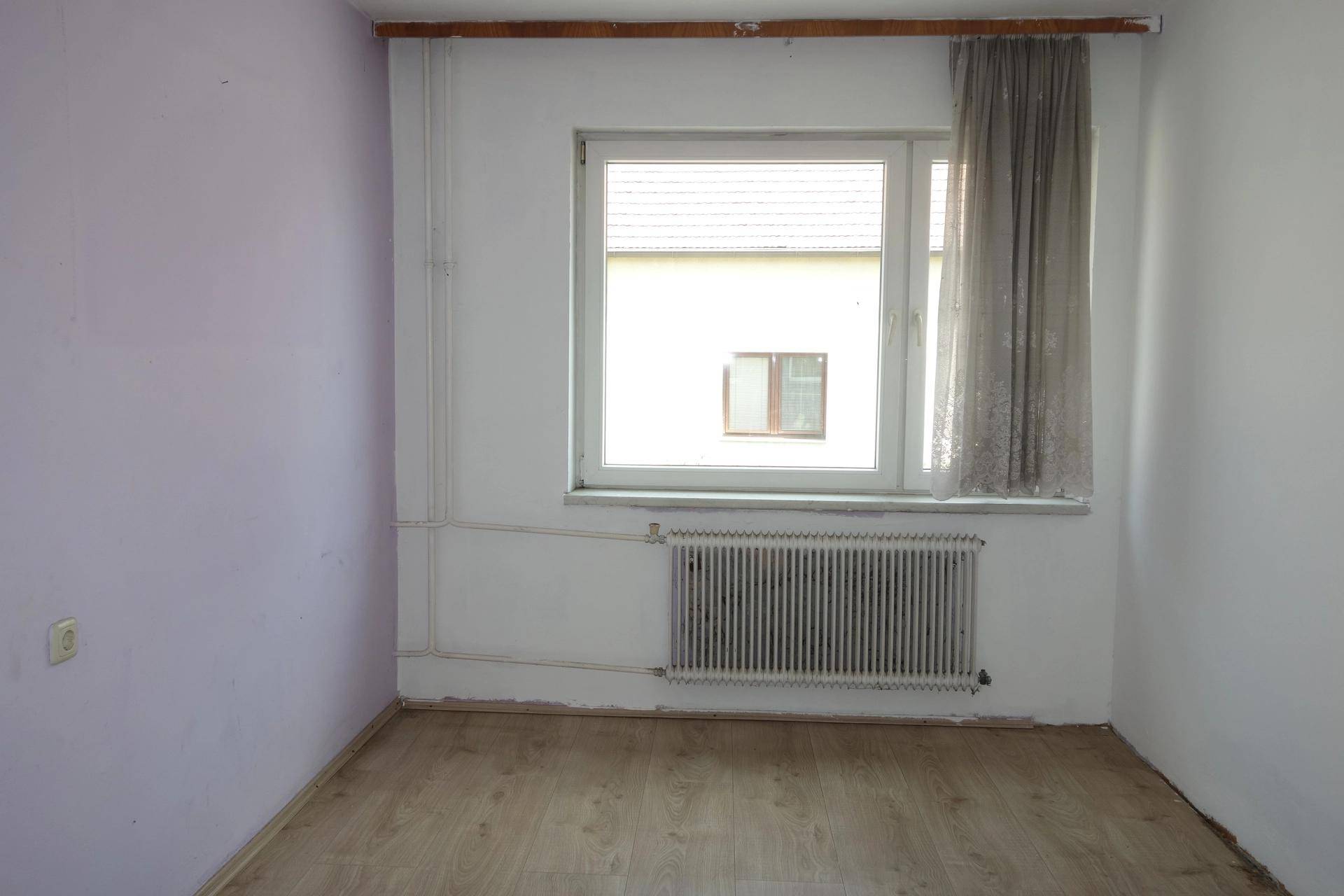 Leeres Zimmer mit hellvioletten Wänden, Laminatboden, Fenster und Heizkörper.