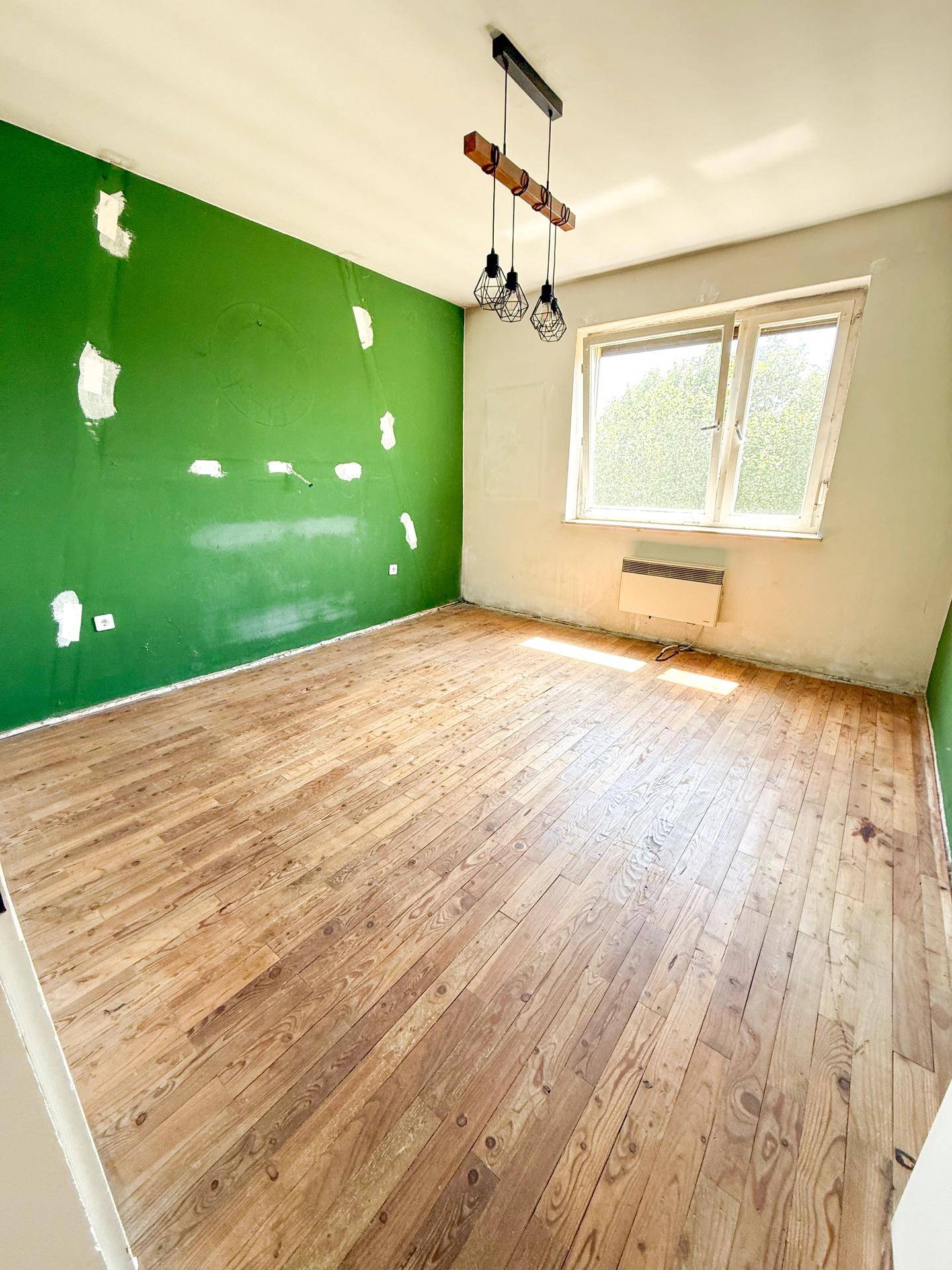 Leeres Zimmer mit grüner Wand, Holzboden und Fenster, bereit für Renovierungsarbeiten.