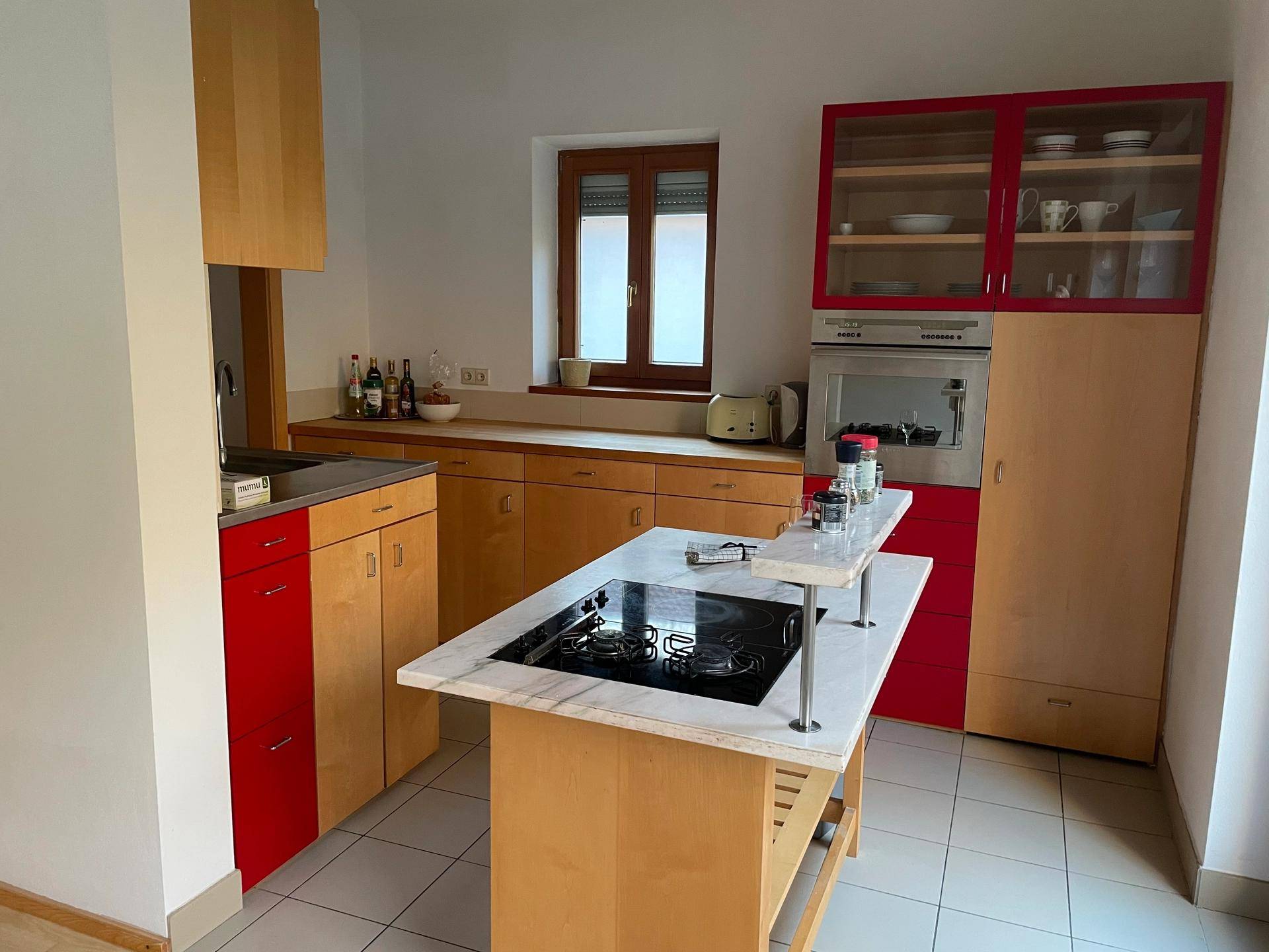 Funktionale Küche mit roten und holzfarbenen Schränken, Kochinsel und Fenster.