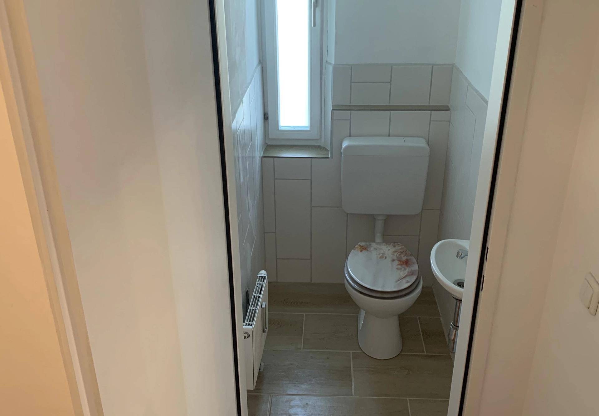 Kleines Gäste-WC mit Fenster, Toilette und einem kompakten Waschbecken.