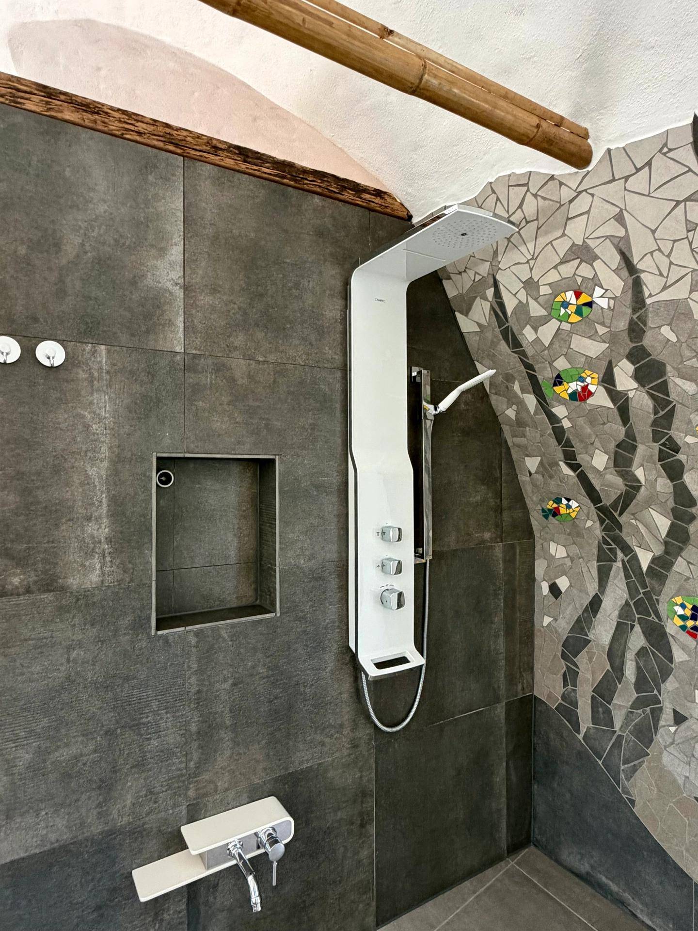 Moderne Dusche mit dunklen Fliesen und dekorativer Mosaikwand, ergänzt durch Bambusdetails.