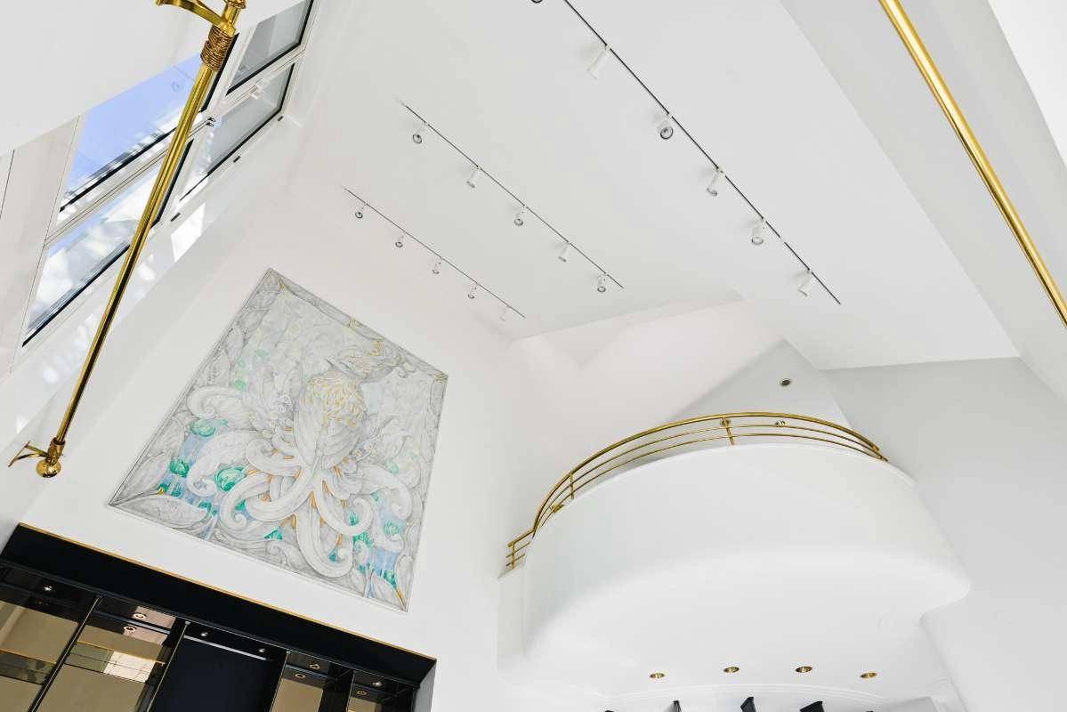 Hoher Deckenbereich mit Oberlichtern, indirekter Beleuchtung und einer Galerie mit goldenem Geländer.