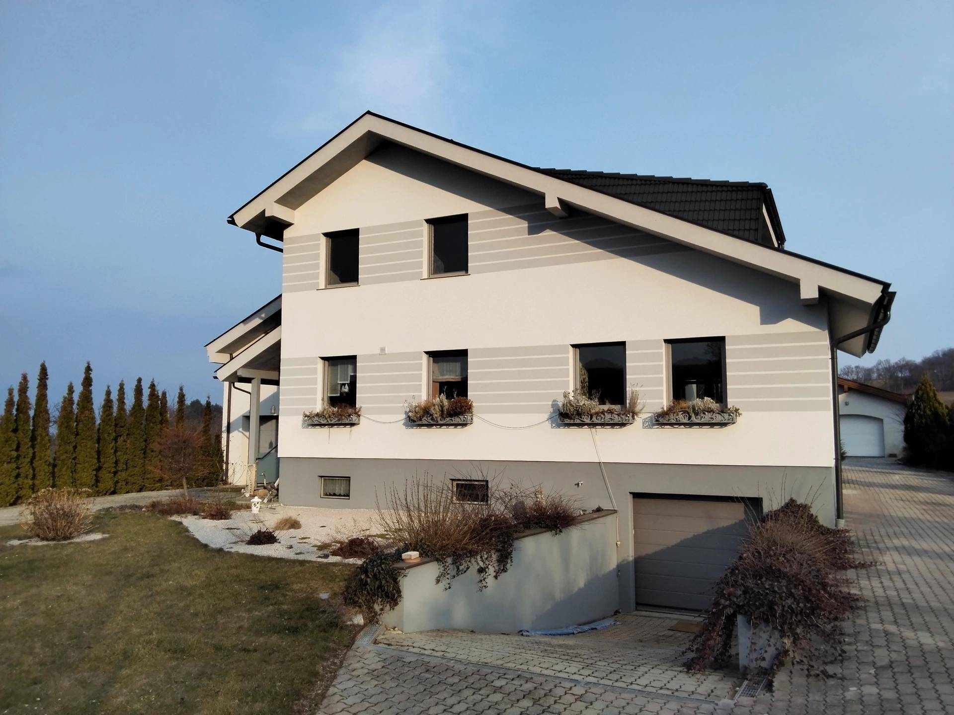 Seitenansicht des Hauses mit Satteldach, Blumenkästen und Zufahrt zur Tiefgarage.