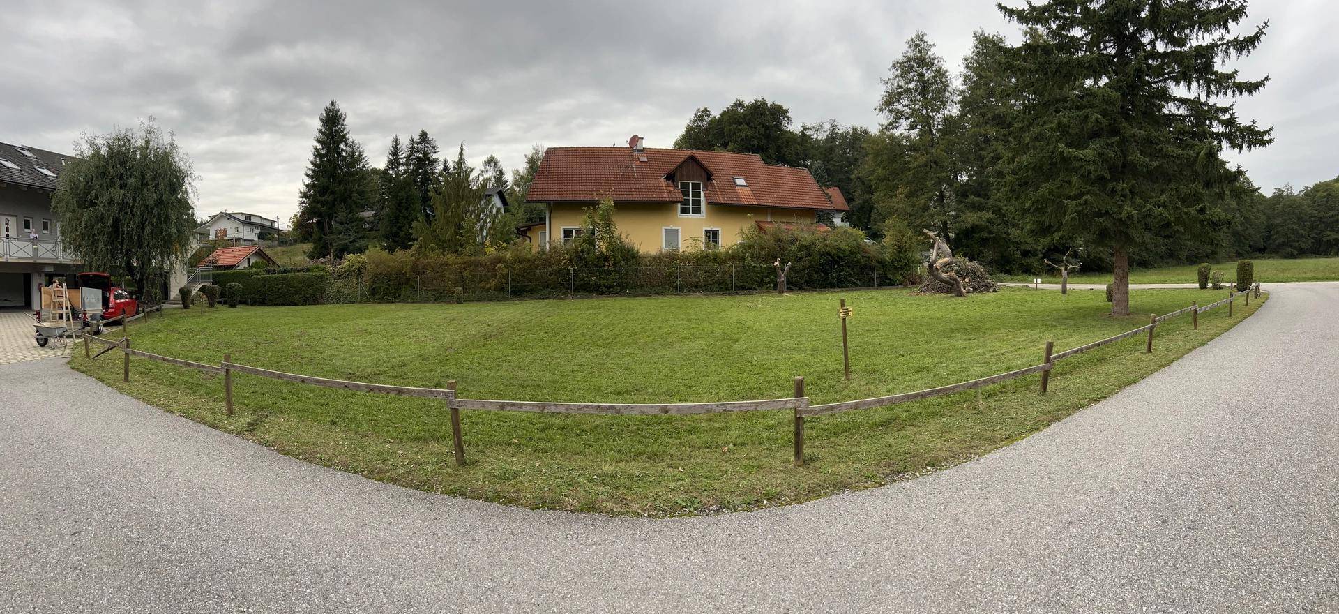 Weitläufiges grünes Grundstück mit einem gelben Haus im Hintergrund und einfacher Holzzaunbegrenzung.