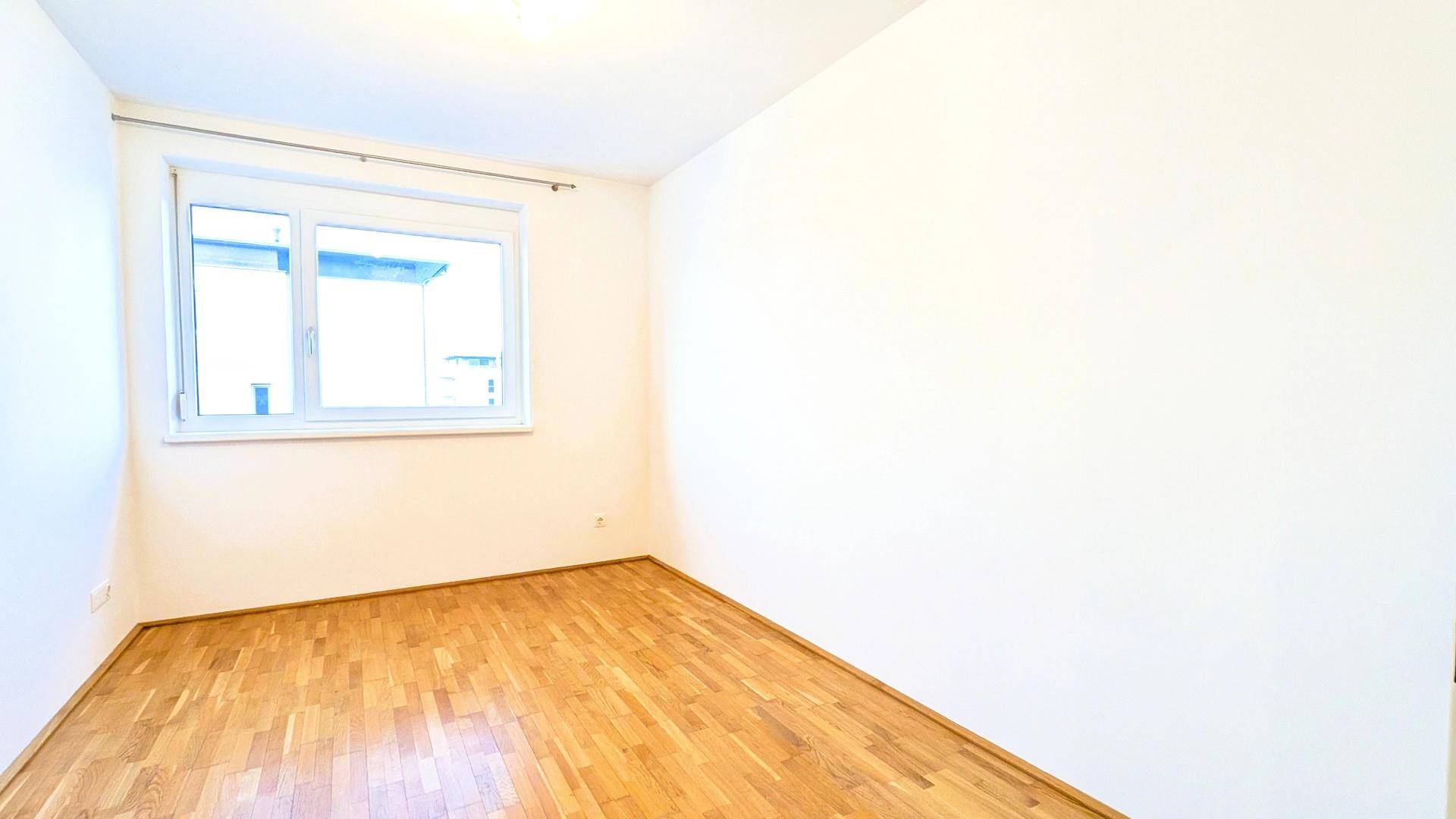 Leeres Zimmer mit Holzboden und Fenster, vielseitig nutzbar als Schlaf- oder Arbeitszimmer.