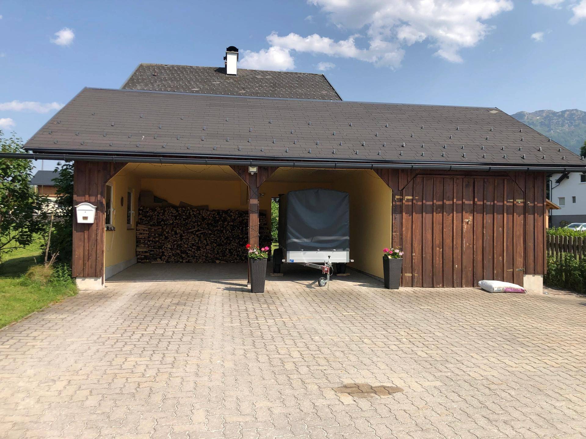 Geräumiger Carport mit Holzlager und gepflasterter Einfahrt.