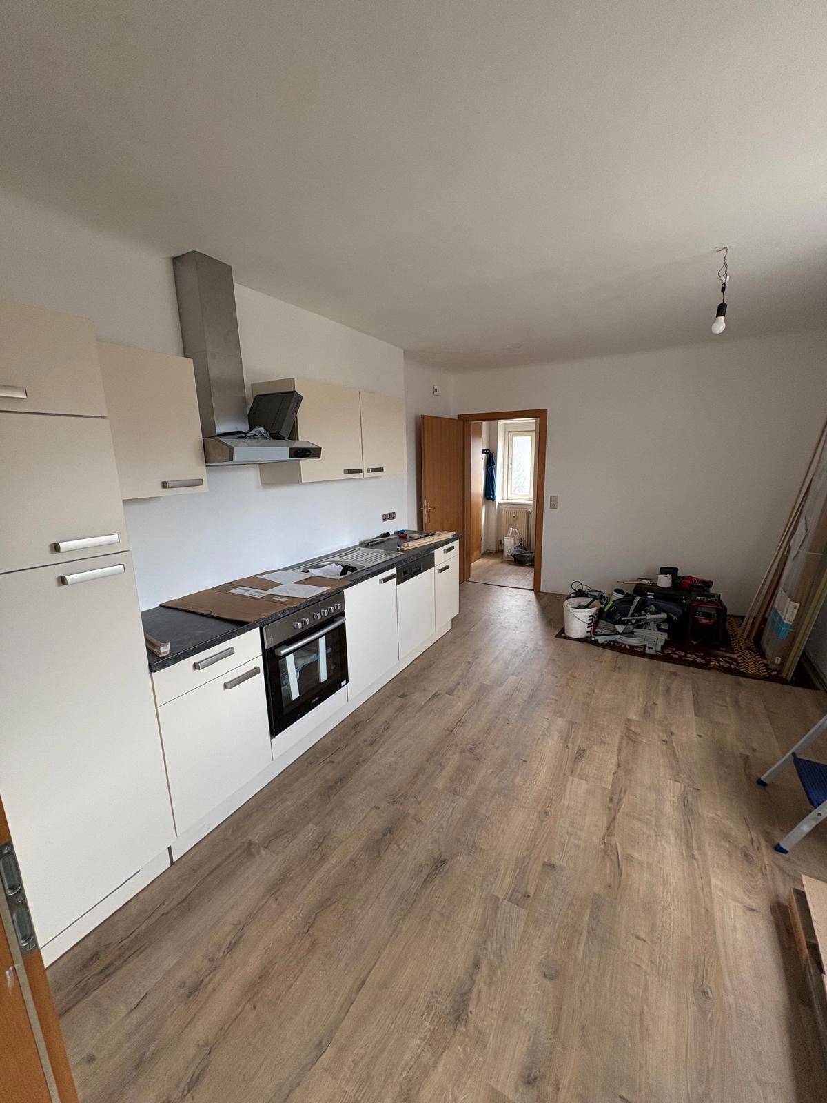 Helle Küche mit Laminatboden und bereits installierten Unterschränken, Backofen und Dunstabzugshaube.