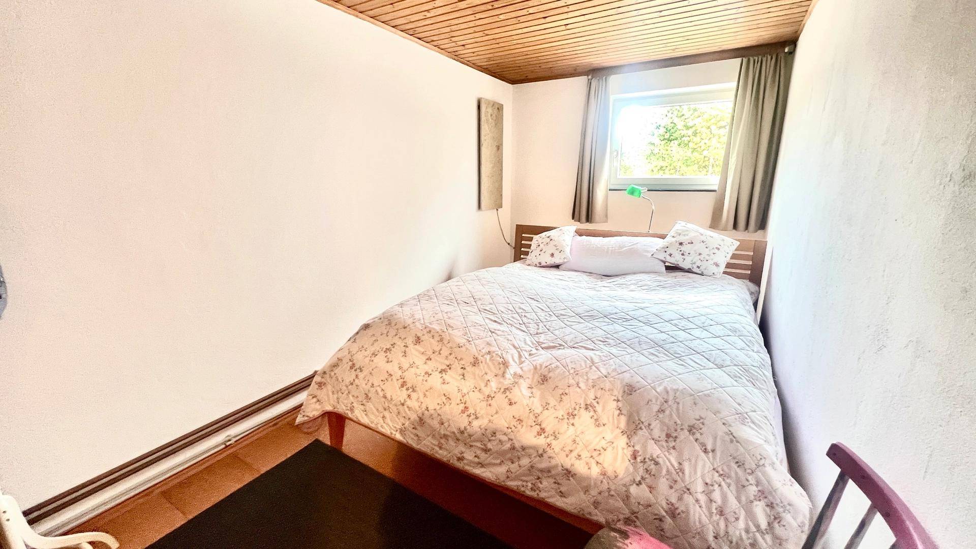 Schlafzimmer mit Doppelbett, weiß gestrichenen Wänden und einem Fenster für Tageslicht.
