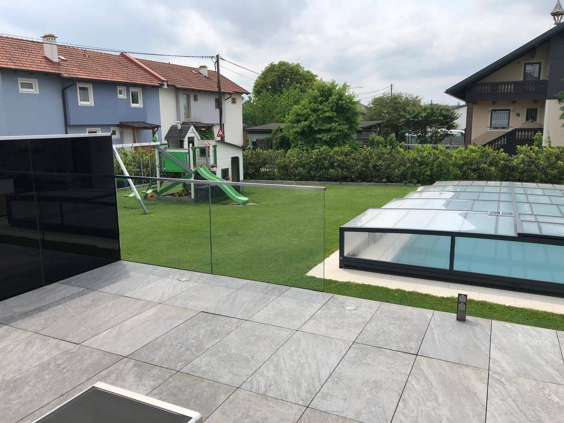 Große gepflasterte Terrasse mit angrenzendem Rasenbereich, Kinderspielplatz und überdachtem Pool.