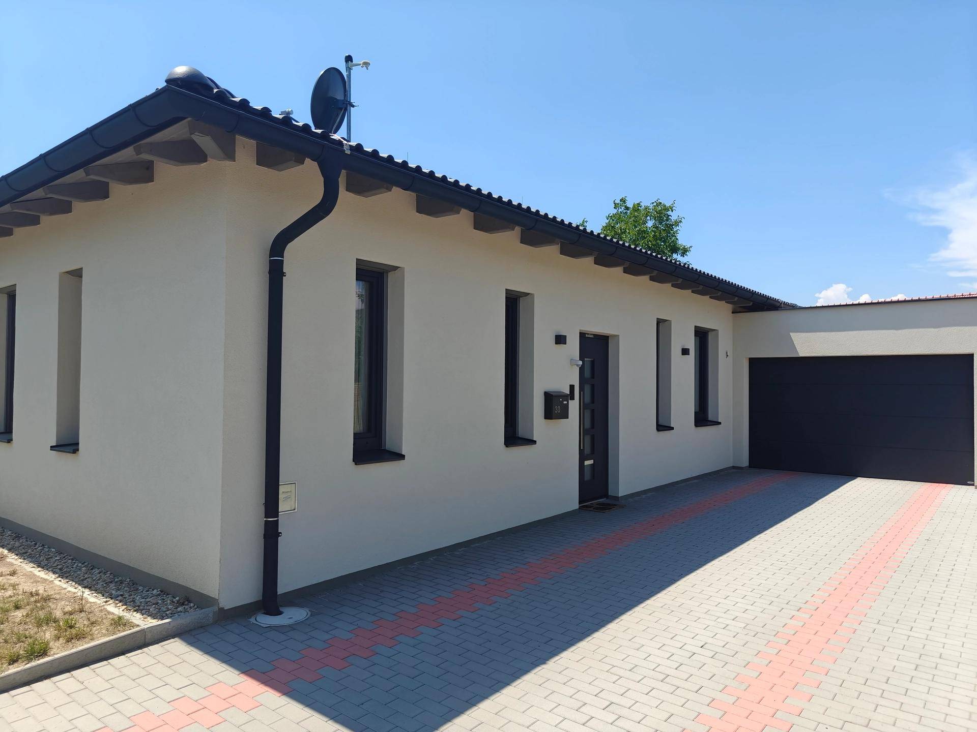 Seitenansicht des Hauses mit gepflasterter Einfahrt und dunklem Garagentor.